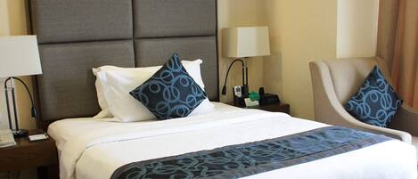 A hotel room with a large bed, two bedside tables, a chair, and a lamp.