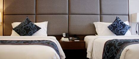 Habitación de hotel con dos camas, cada una con almohada y una mesita de noche con teléfono y lámpara.