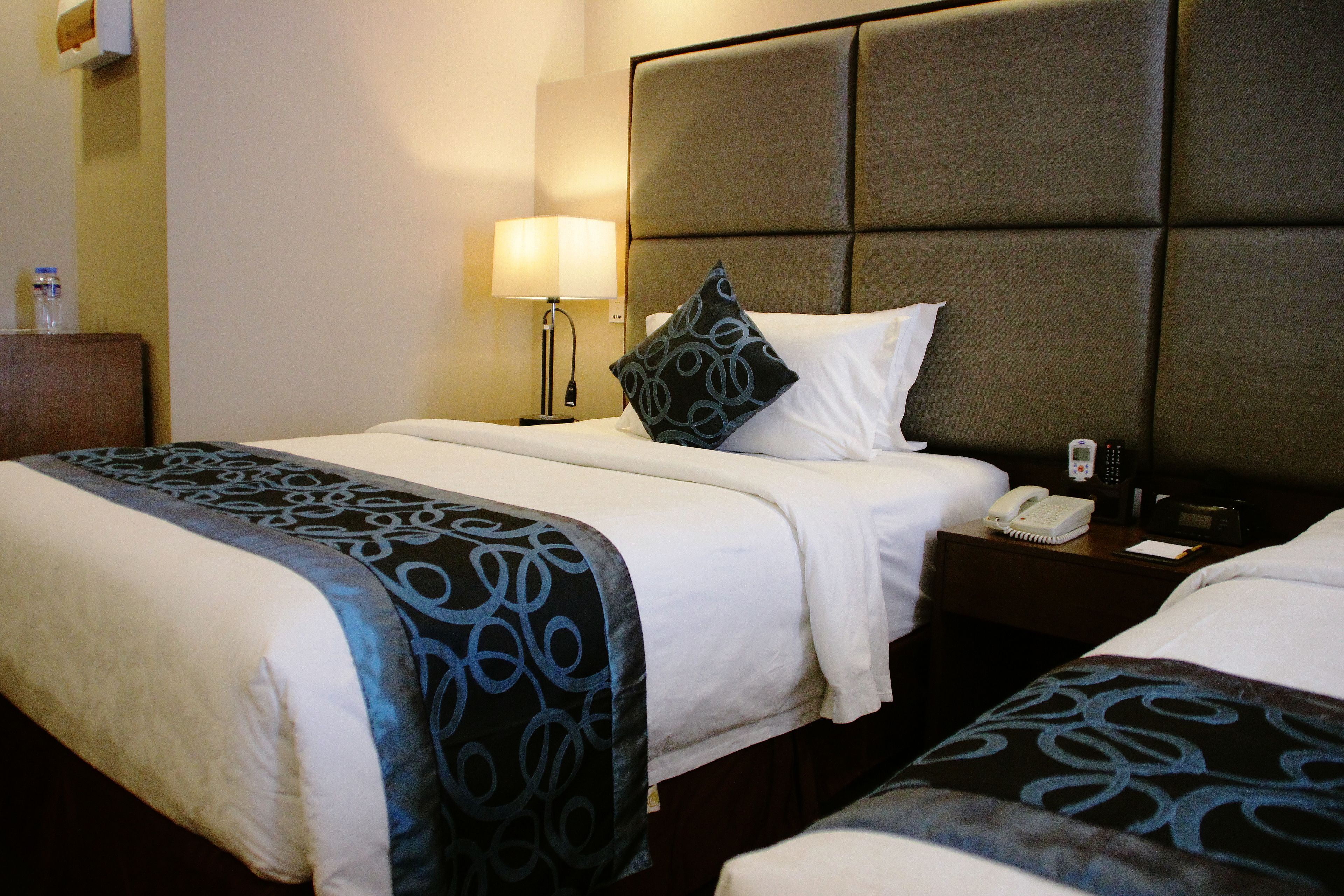 A hotel room with two beds, a nightstand with a lamp, a phone, and a small table.