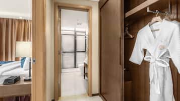 Een hotelkamer met een bed, nachtkastje, lamp en een houten garderobe met daaraan jassen.