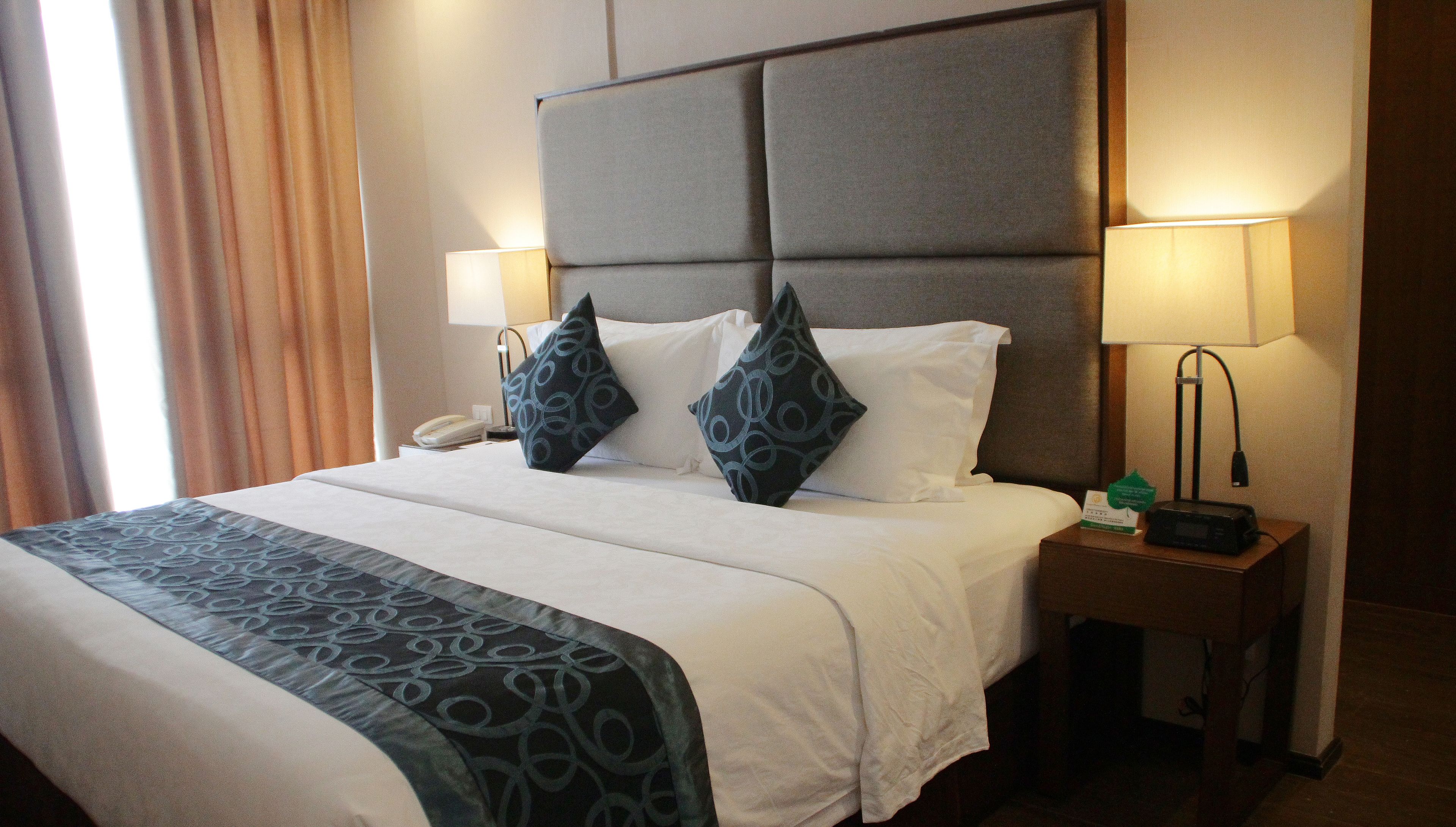 A hotel room with a large bed, two bedside lamps, a telephone, and a small table with a lamp.