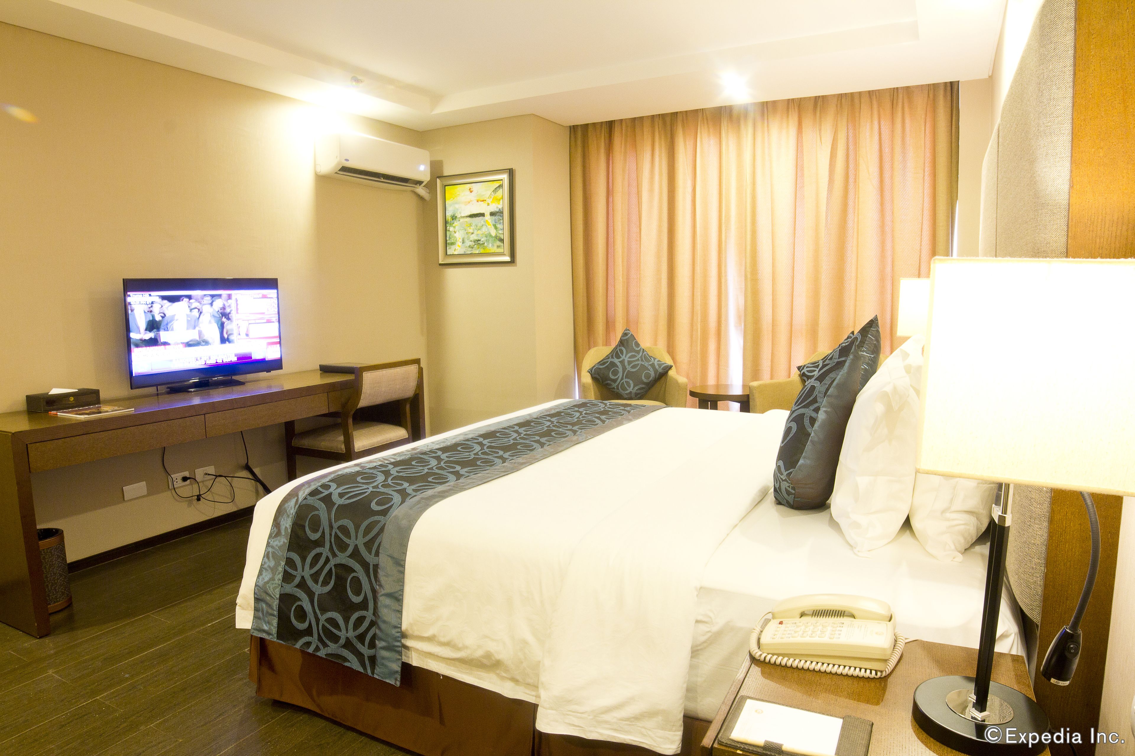 A hotel room with a bed, a desk with a television, a lamp, and a telephone.
