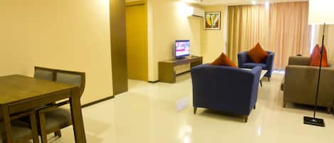 Una habitación de hotel con una mesa de comedor, dos sofás, un televisor y una lámpara.