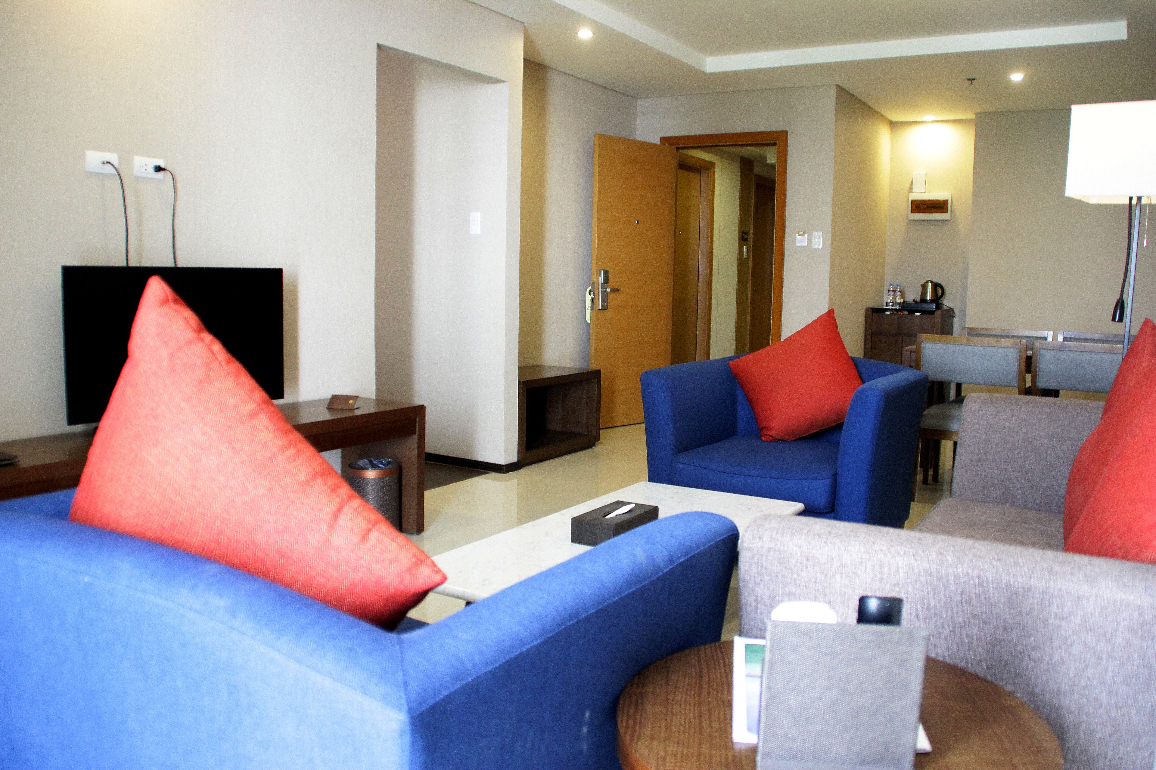 Ein modernes Hotelzimmer mit einem blauen Sofa, roten Kissen, einem kleinen Tisch und einem Fernseher.