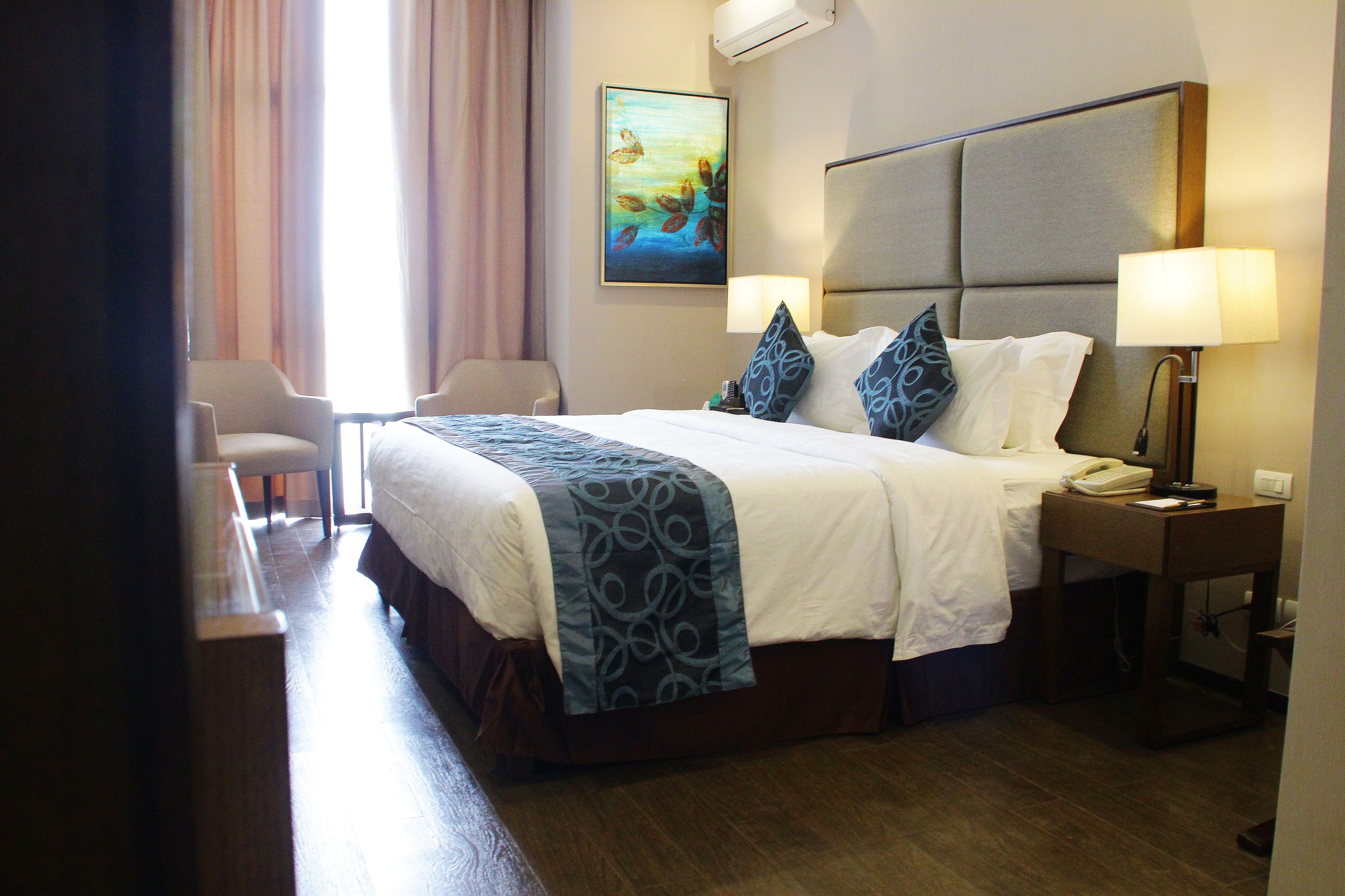 Une chambre d’hôtel avec un grand lit, deux lampes de chevet, un bureau avec un téléphone et une chaise.