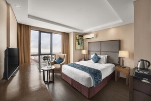A hotel room with a large bed, a desk, a chair, a TV, a coffee maker, and a window with a view. - Golden Phoenix Hotel Manila (Pasay)