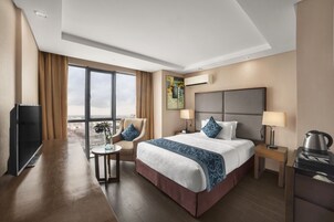 Une chambre d’hôtel avec un grand lit, un bureau, une chaise, une télévision, une machine à café et une fenêtre donnant sur un beau paysage.