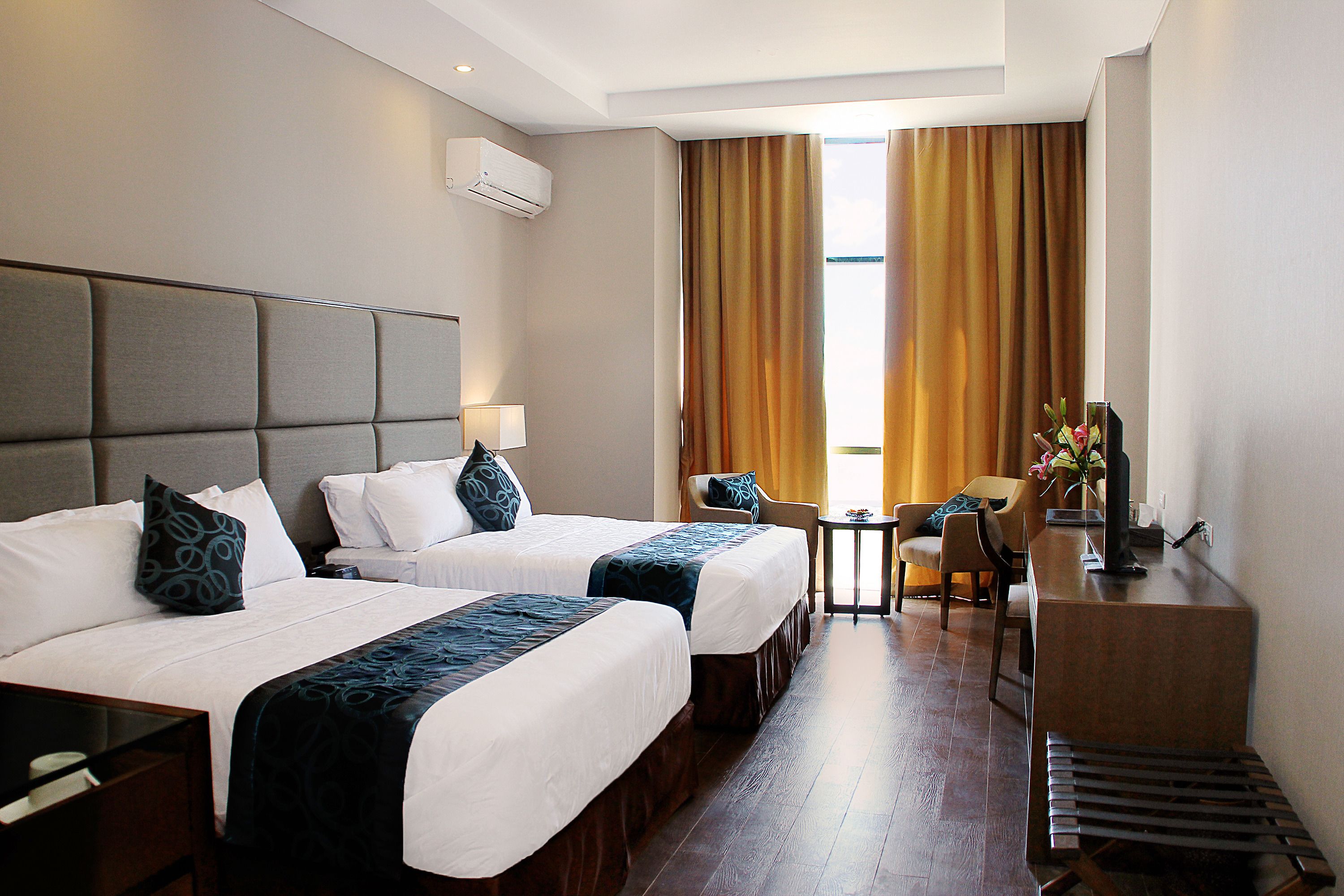 A hotel room with two beds, a desk, a chair, and a small table.