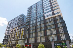 Un immeuble à plusieurs étages doté d’une architecture moderne, caractérisé par un mélange de façades en verre et en métal, et abritant plusieurs commerces au rez-de-chaussée.