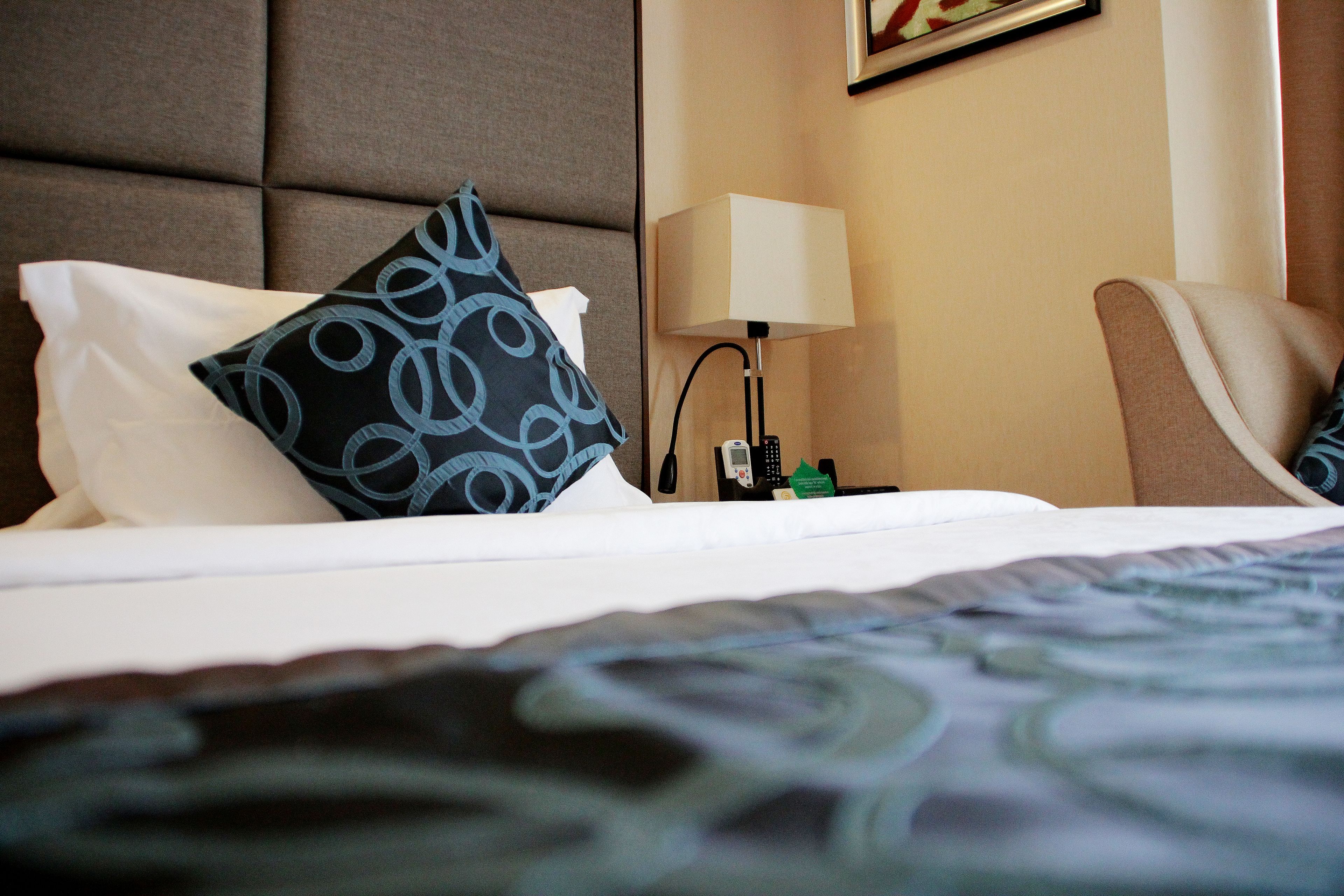 Una camera d'albergo con un letto, un cuscino, una lampada da comodino e una sedia.