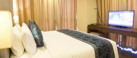 A hotel room with a bed, a television, and a desk.