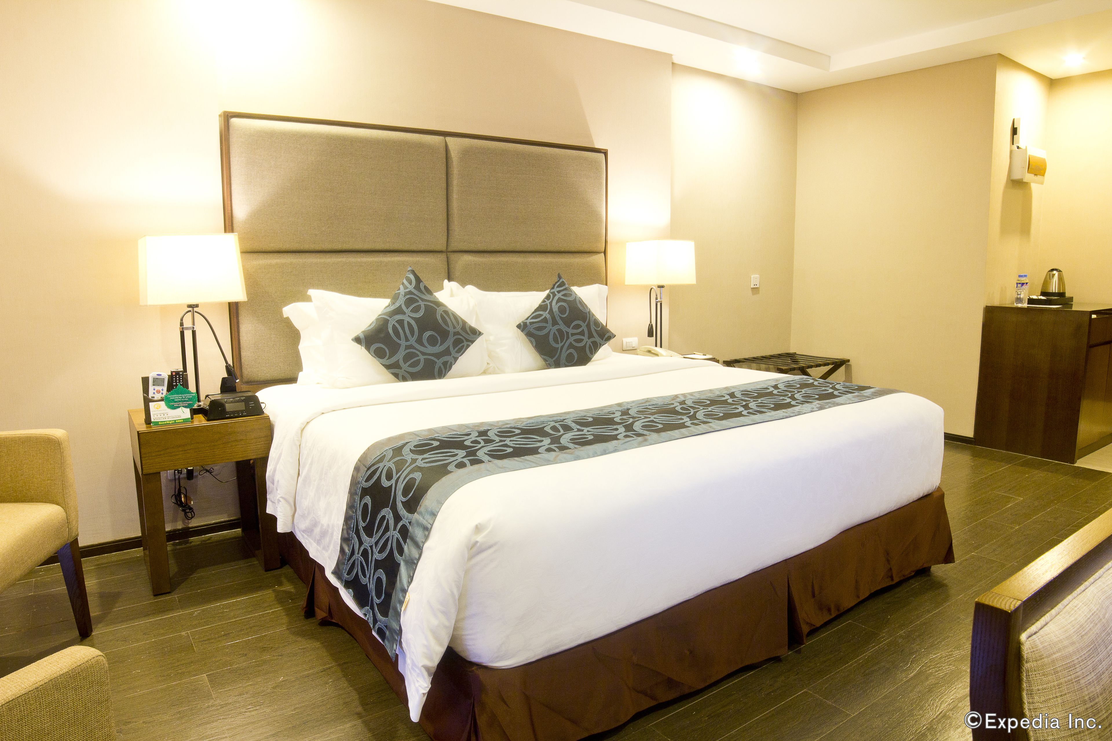 Una habitación de hotel con una cama grande, dos mesitas de noche con lámparas, una silla de madera y un escritorio con teléfono.
