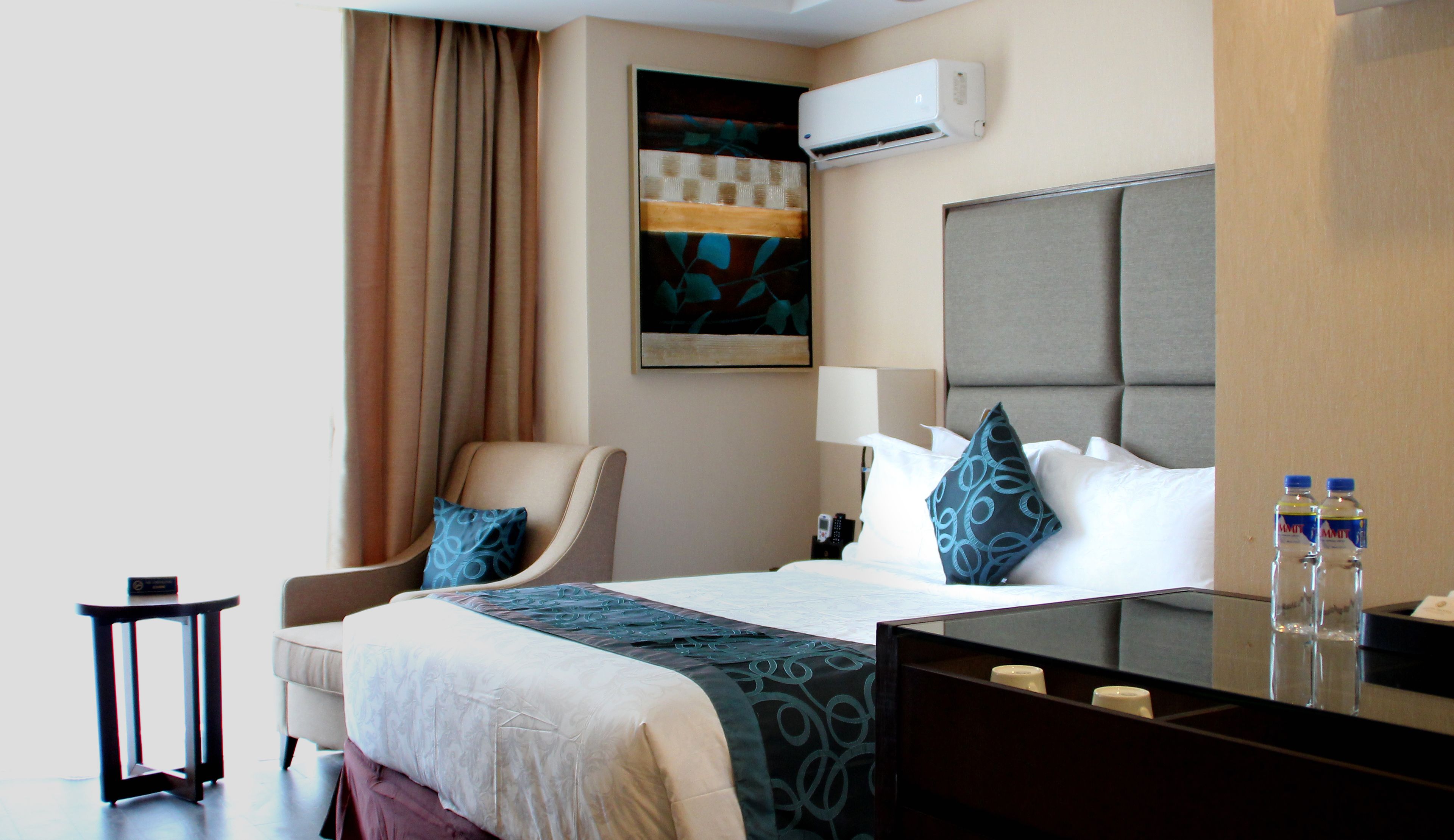 Habitación de hotel con cama, una silla, una mesita de noche, un equipo de aire acondicionado y un cuadro en la pared.