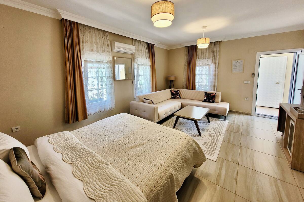 A hotel room with a large bed, a sofa, a small table, and a door leading to a balcony.
