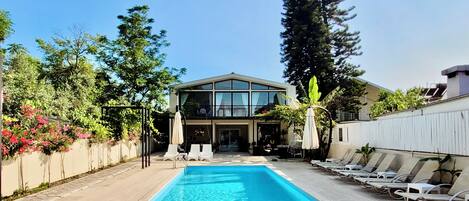 A swimming pool with lounge chairs, a two-story building with large windows, and surrounding greenery.