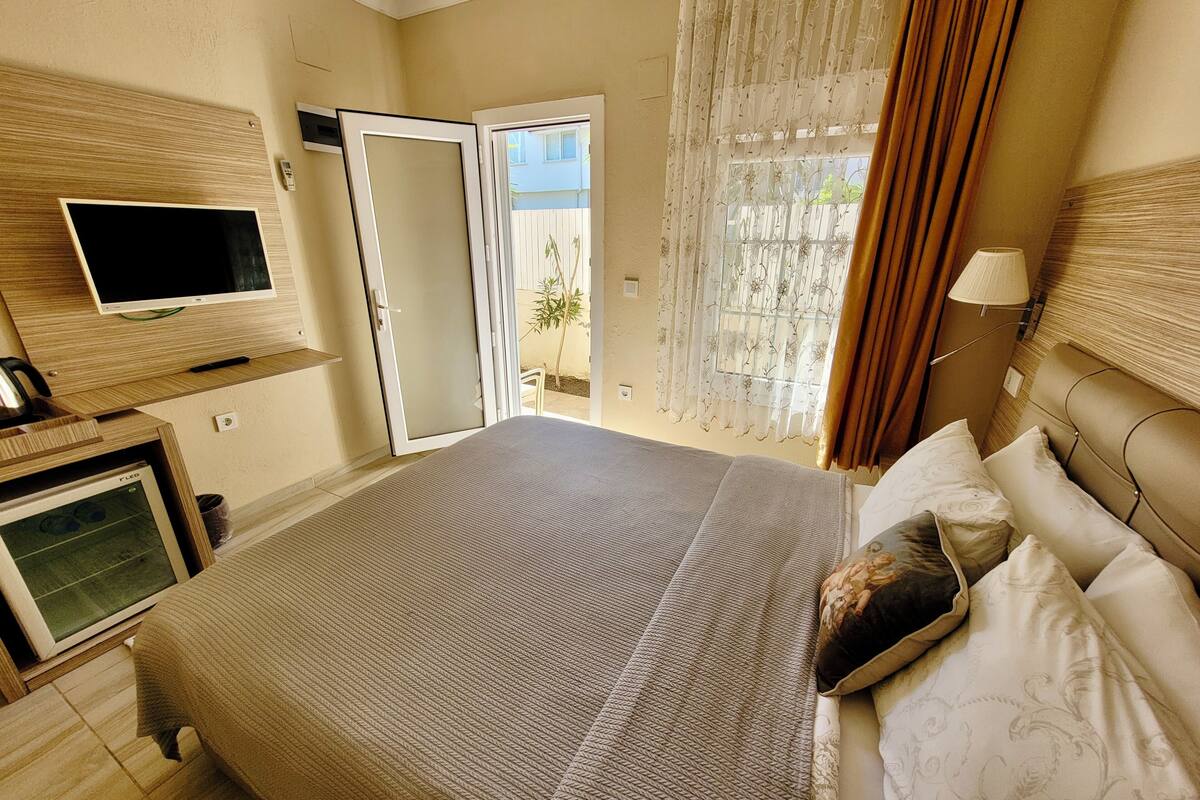A hotel room with a bed, a television, a desk with a computer, and a window with curtains.