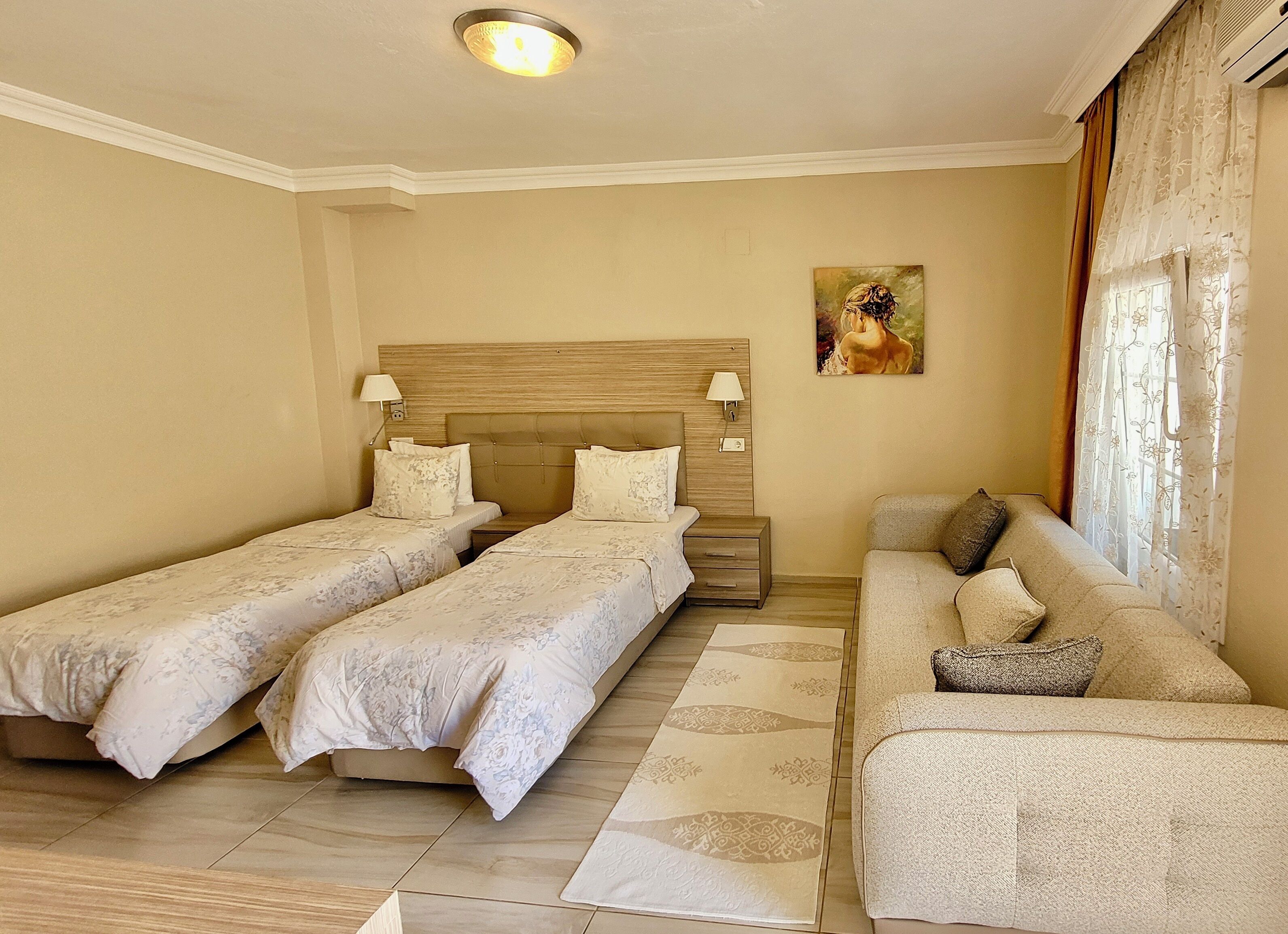 A hotel room with two single beds, a sofa, a nightstand, and a painting on the wall.
