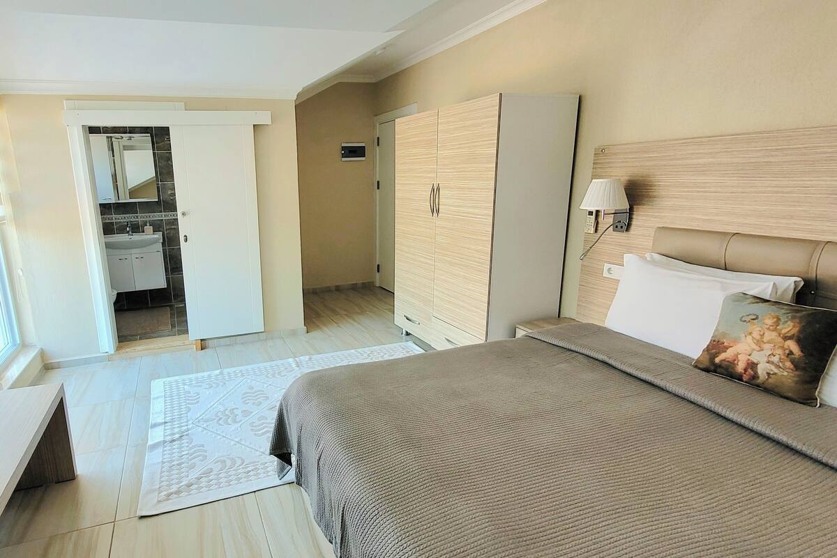 A hotel room with a bed, bedside table, lamp, and a view of the bathroom.