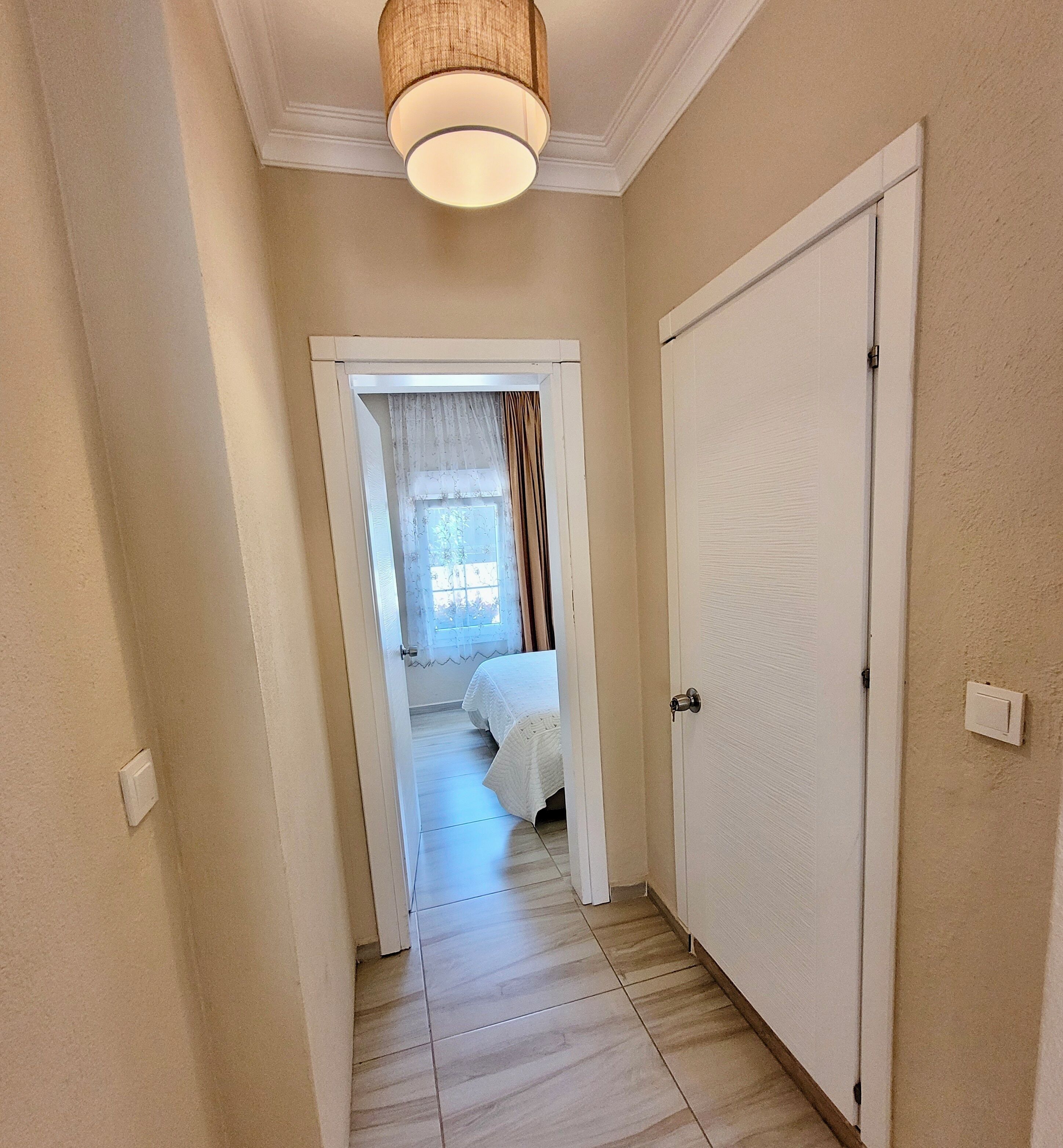 A hallway with a door leading to a bedroom with a bed and a window.