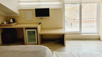 Un dormitorio con cama, escritorio con computadora, televisor y ventana con persianas.