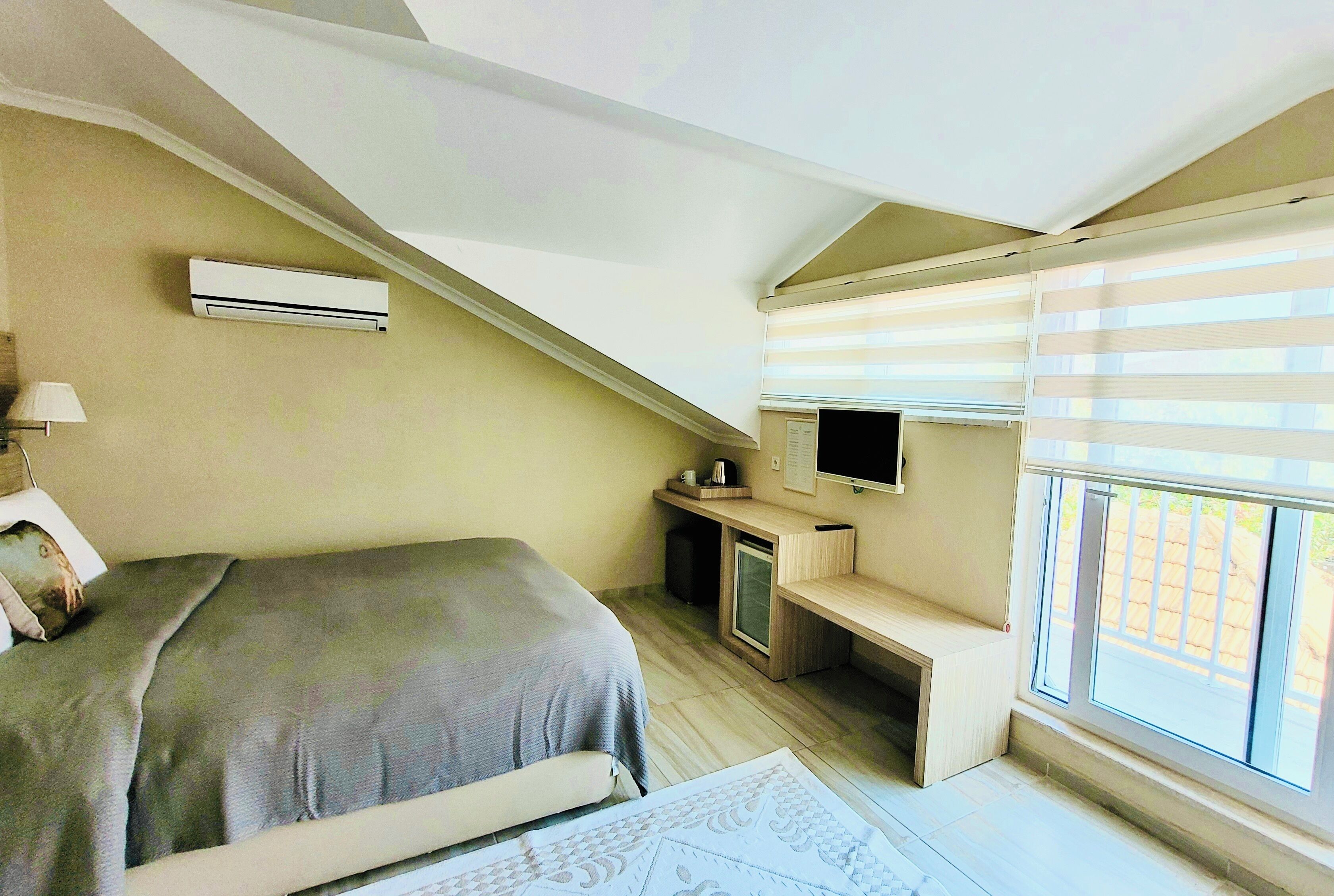 A bedroom with a bed, a desk, a television, and an air conditioning unit.