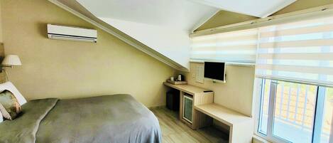 A bedroom with a bed, a desk, a television, and an air conditioning unit.