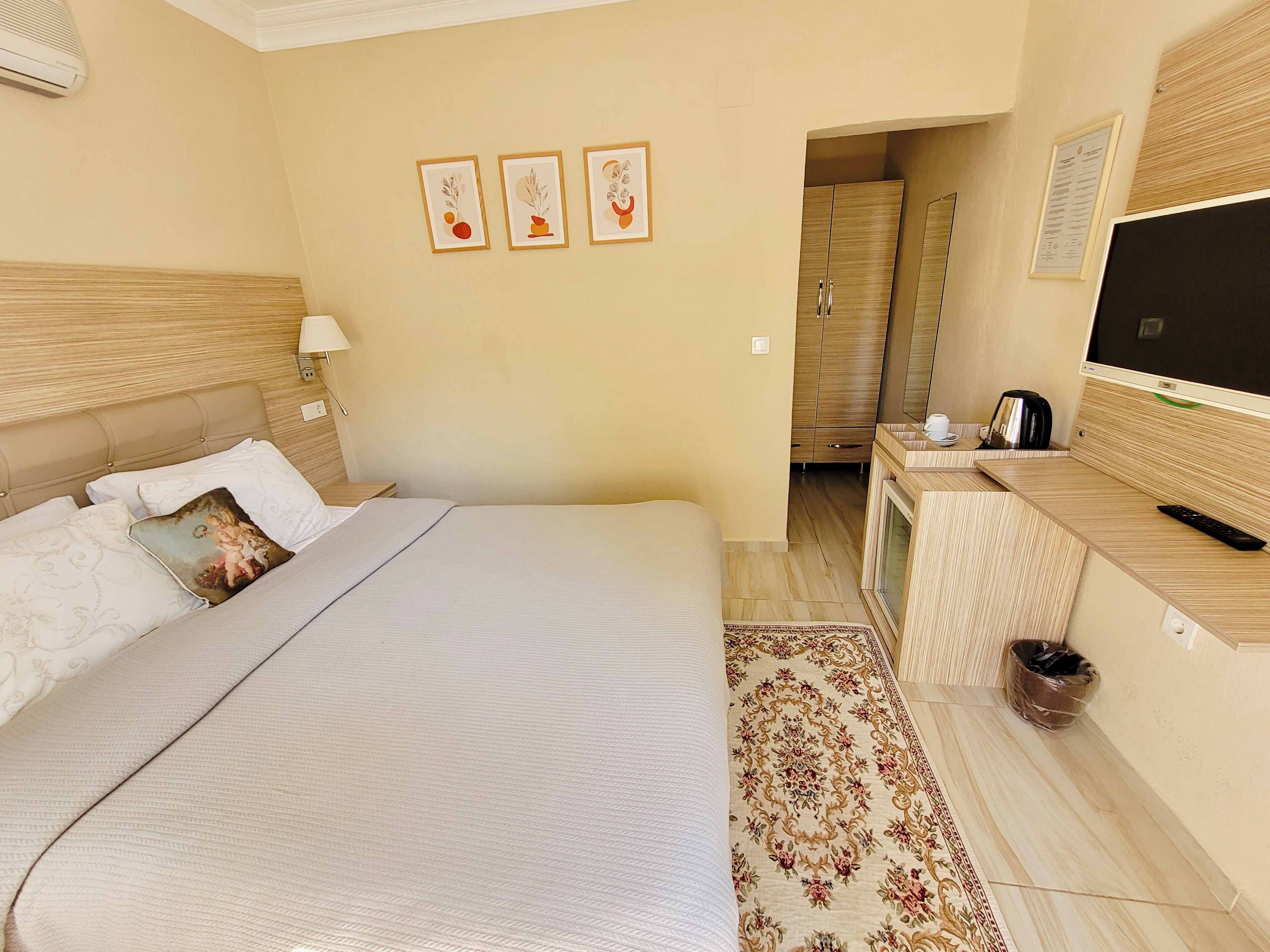 A hotel room with a bed, a desk with a TV, a coffee maker, and a trash bin.