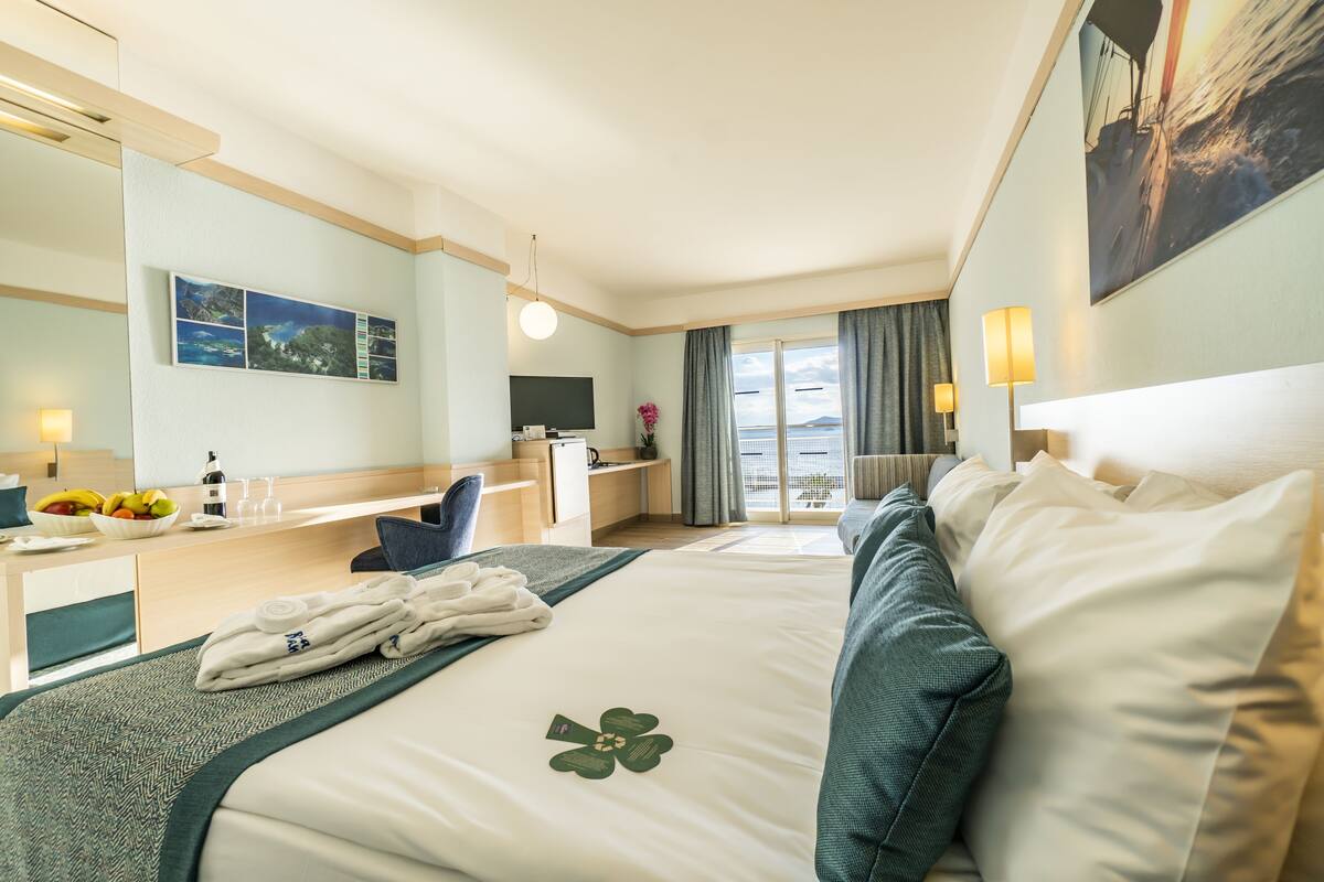 Quarto de hotel com cama, escrivaninha, cadeira, televisão e vista para o mar.