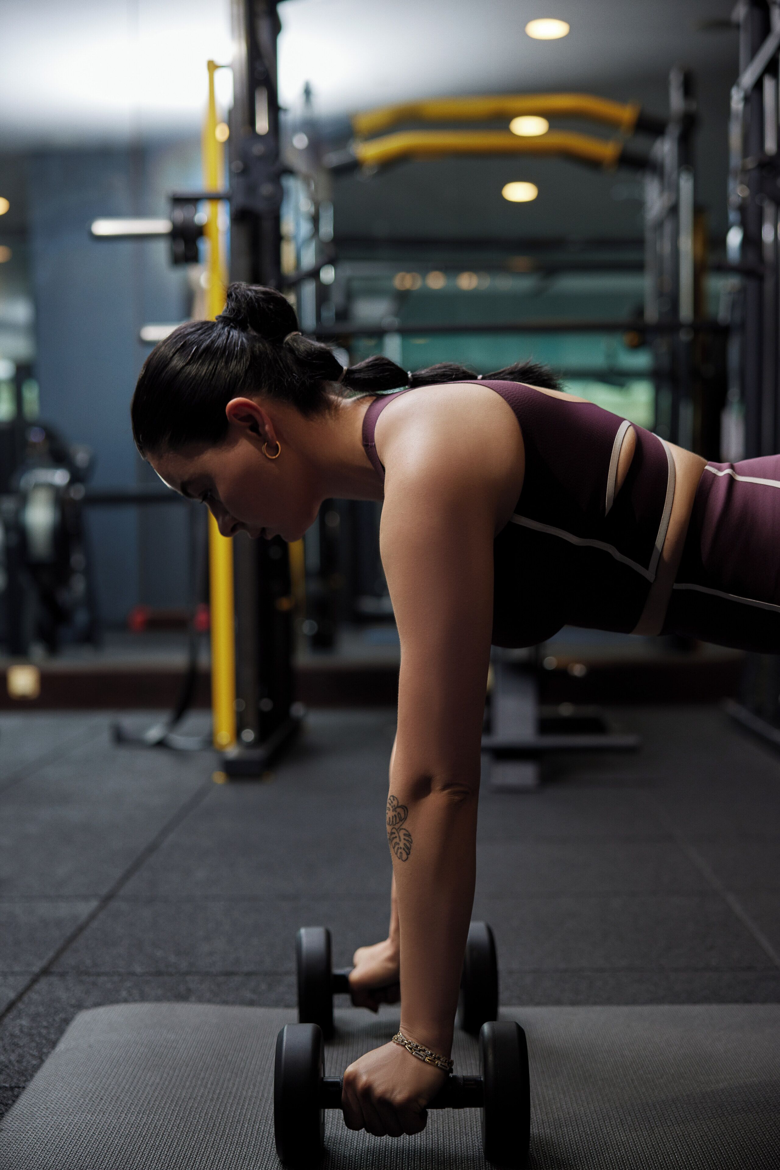 A person performing a dumbbell exercise in a gym with exercise equipment in the background.