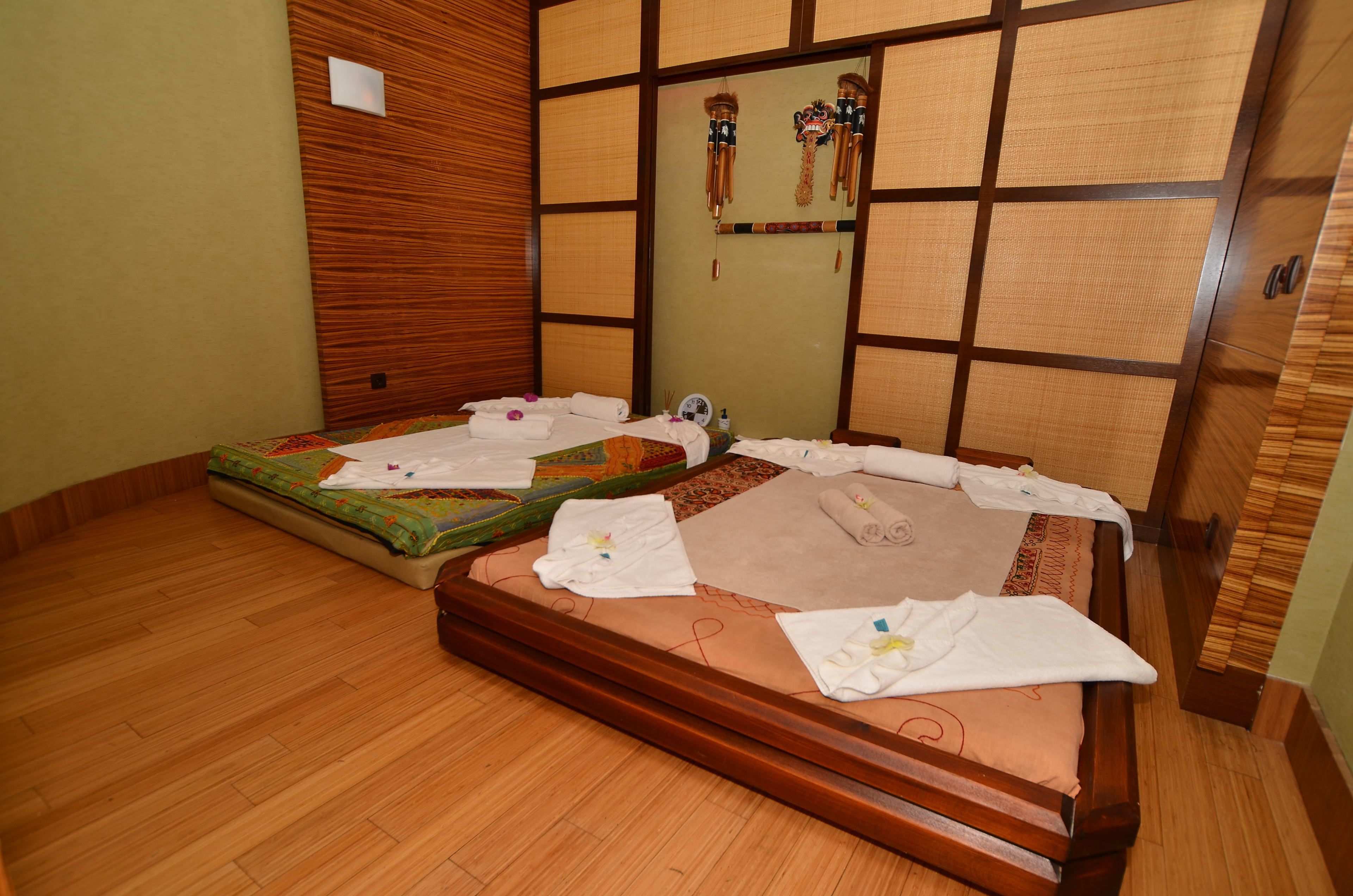 A room with two wooden beds, each with a mattress, pillows, and towels.