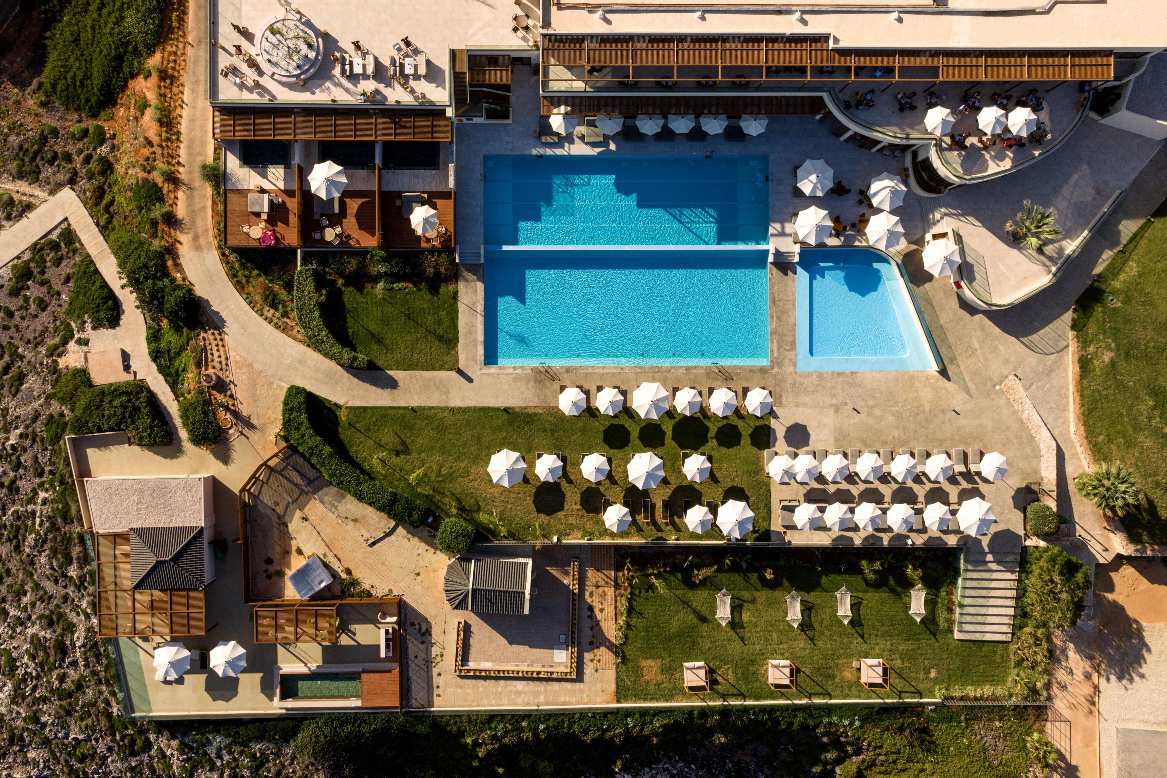 Vue aérienne d’un complexe hôtelier doté de plusieurs piscines, de chaises longues et d’une pelouse bien entretenue.