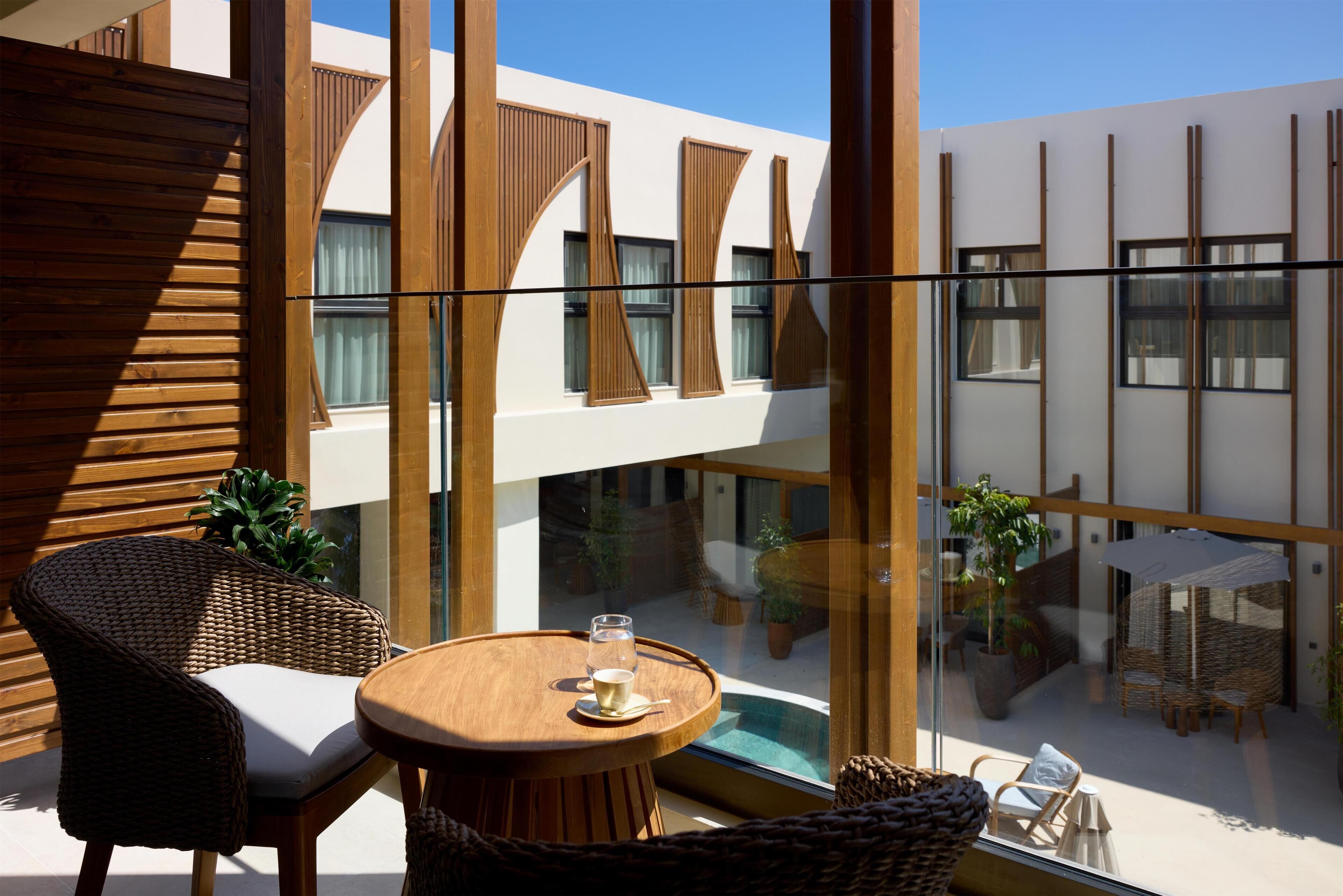 Un balcon agrémenté de meubles en osier, d’une table en verre et offrant une vue sur une piscine et un espace de détente intérieur.