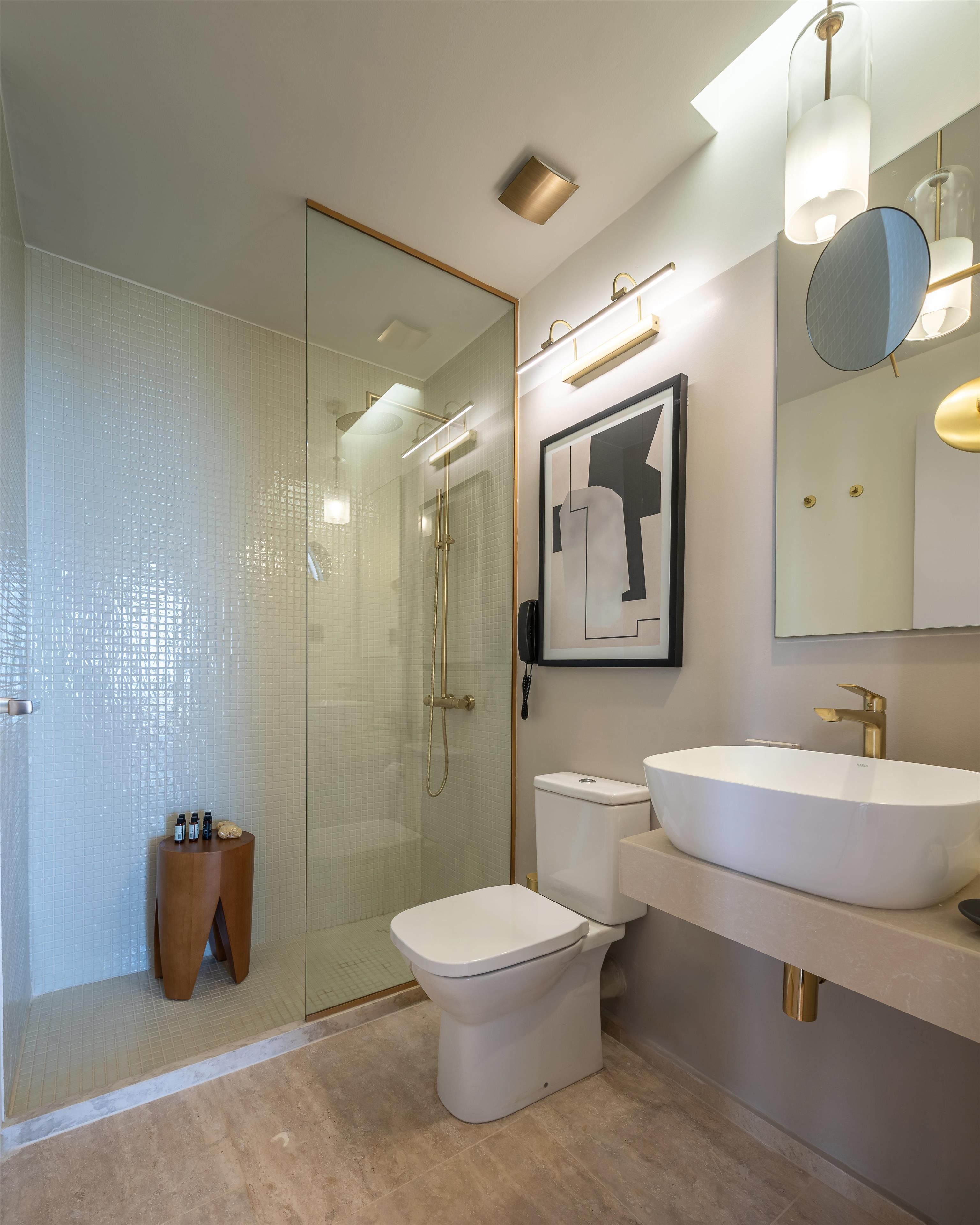 A modern bathroom with a glass shower enclosure, a toilet, a sink, and a framed artwork on the wall.