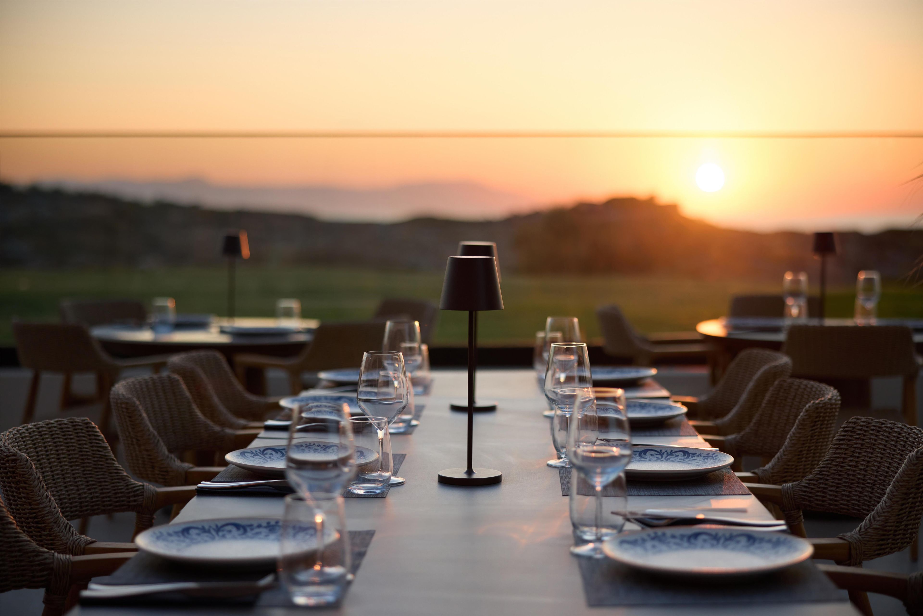 Een gedekte tafel klaar voor een diner, met helder glaswerk en borden, gericht op een prachtig uitzicht bij zonsondergang.