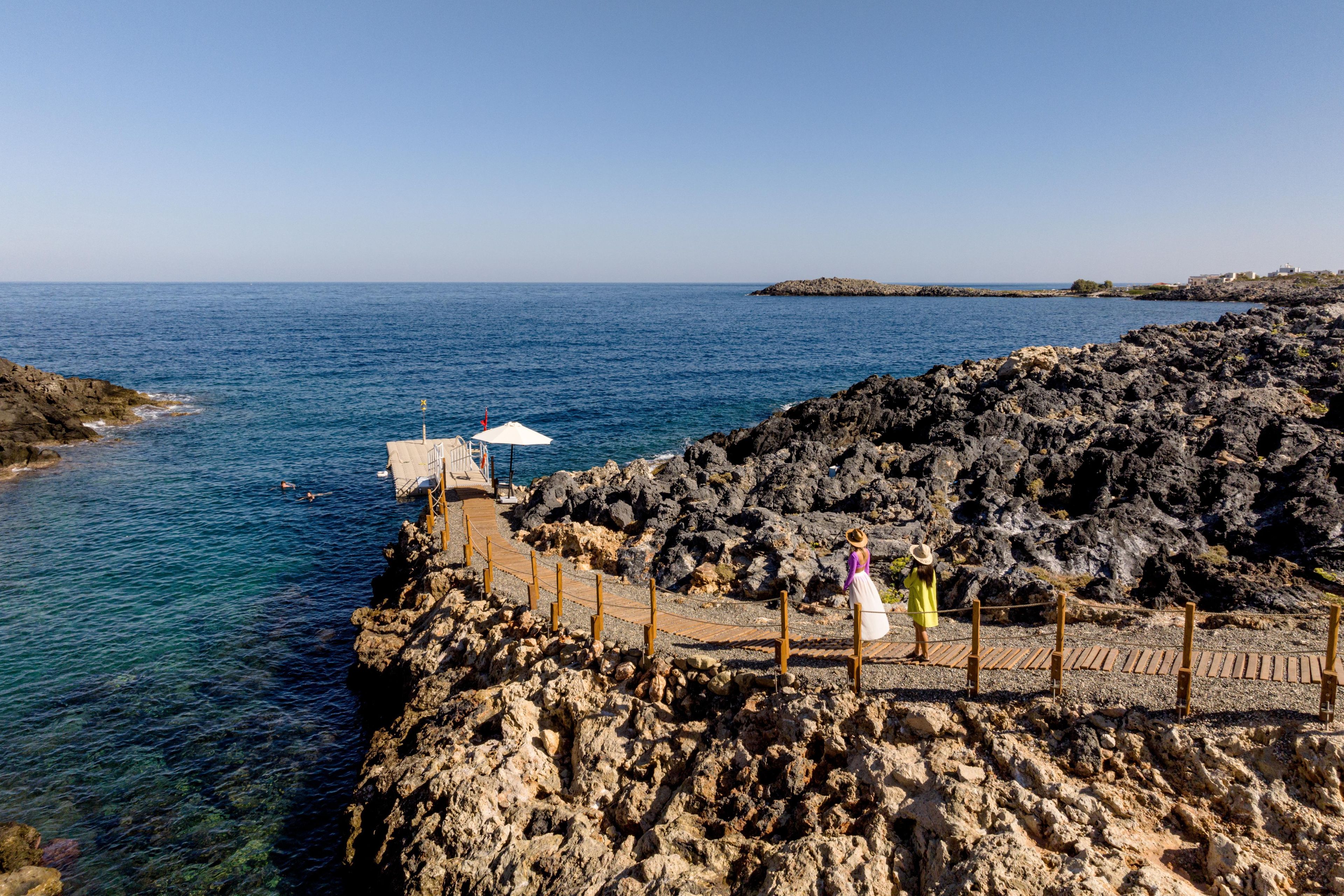 A rocky coastline with a wooden walkway leading to a white structure with an umbrella.