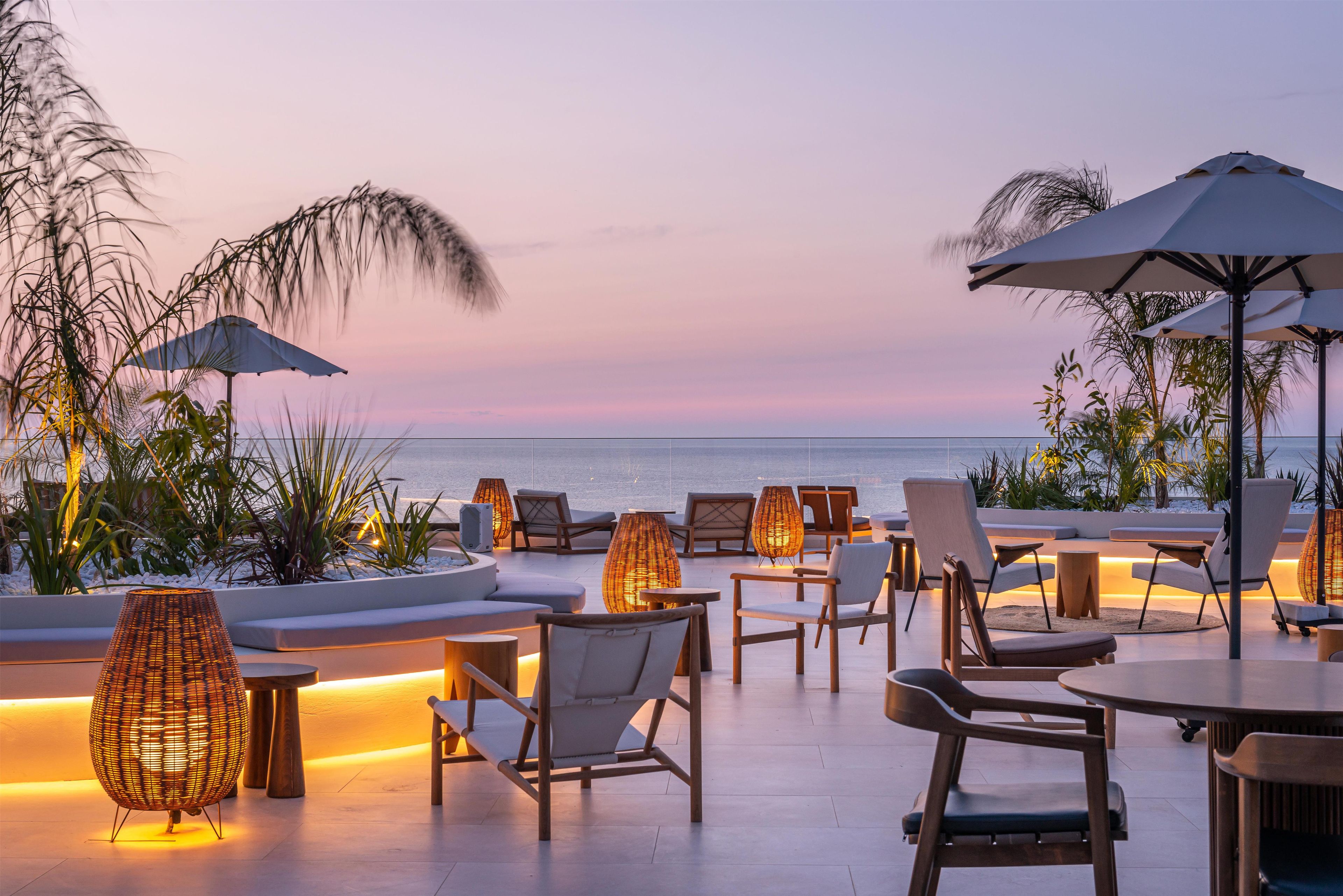 A rooftop terrace with seating, tables, and umbrellas overlooking the ocean.