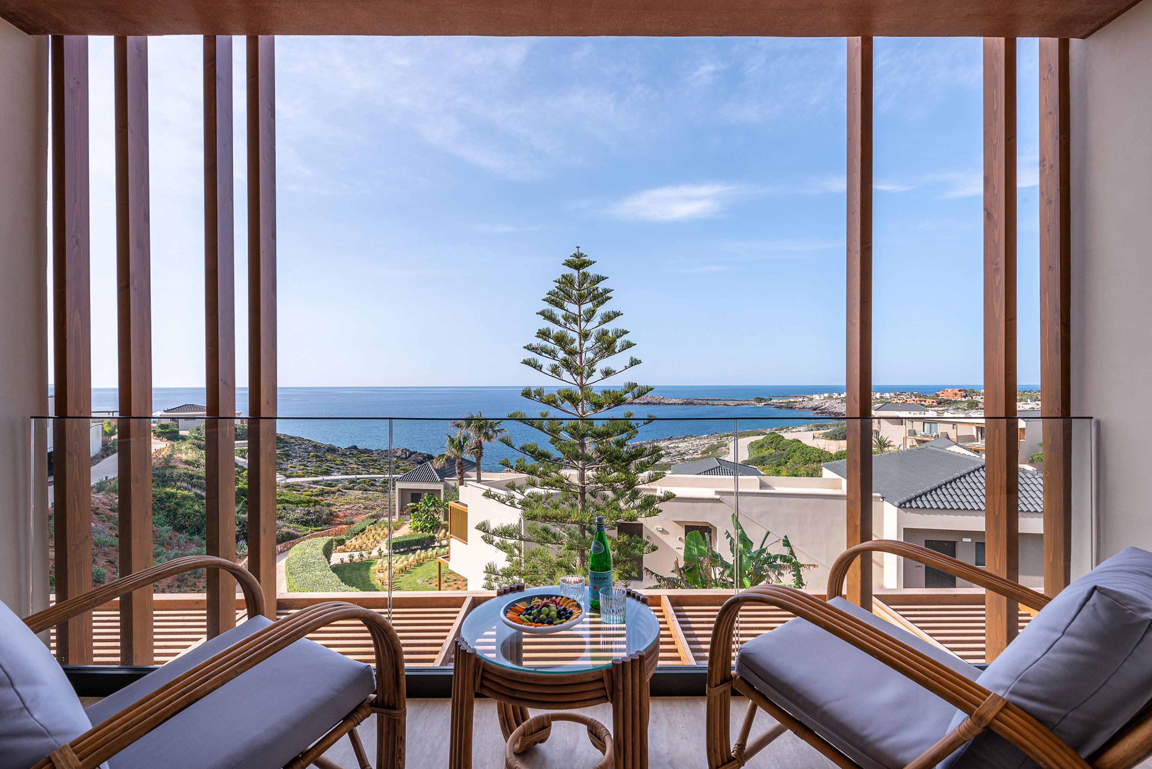 Un balcón con vista al mar, amoblado con sillas de mimbre y una mesa de vidrio.