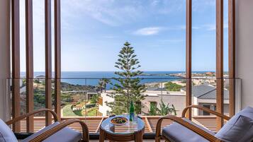 Un balcón con vista al mar, amoblado con sillas de mimbre y una mesa de vidrio.