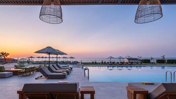 A poolside area with lounge chairs and umbrellas, overlooking a body of water at sunset.