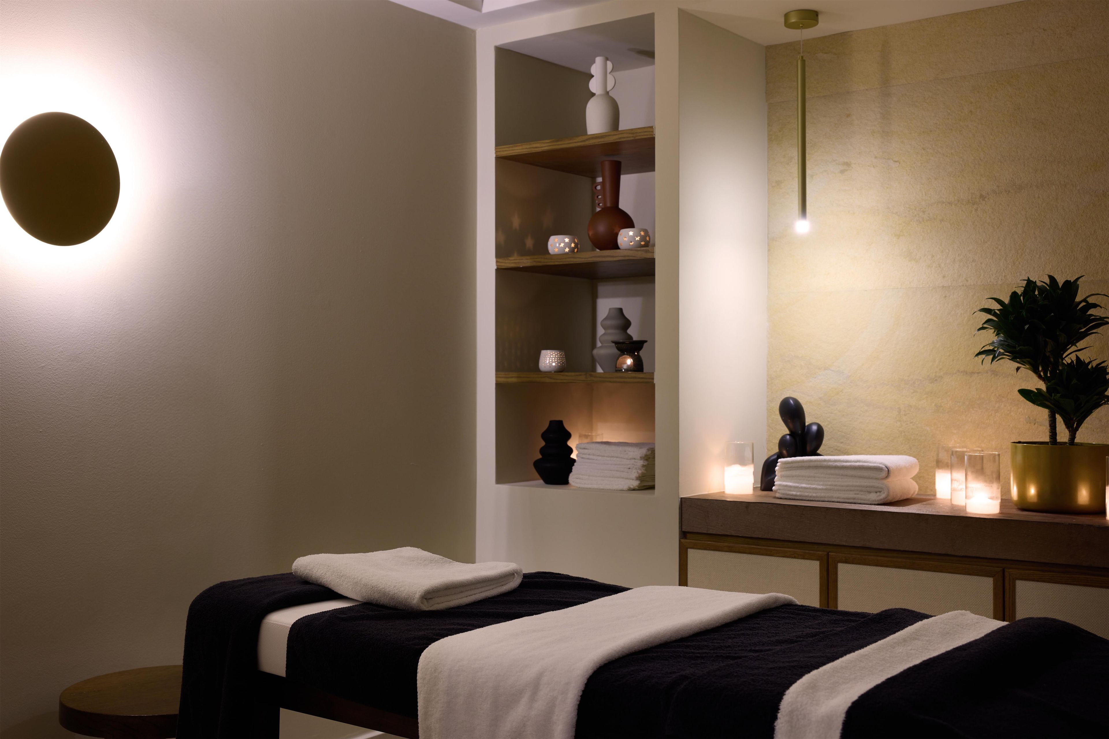 A spa room with a massage table, shelves with decorative items, and a potted plant.