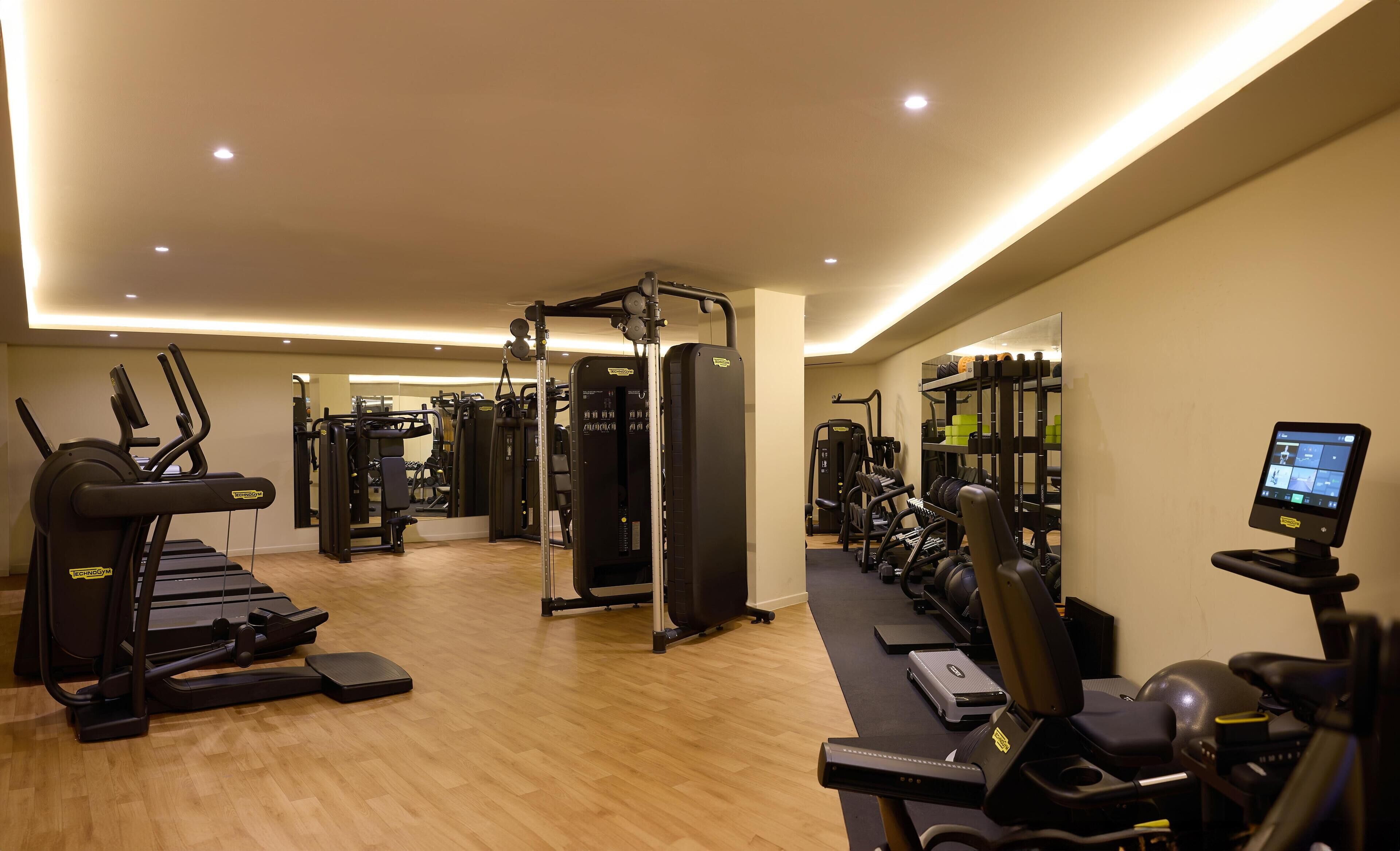 Un gimnasio con cintas de correr, máquinas de pesas y una pantalla digital.