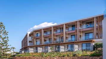 A modern multi-story hotel with balconies, stone facade, and landscaped gardens.
