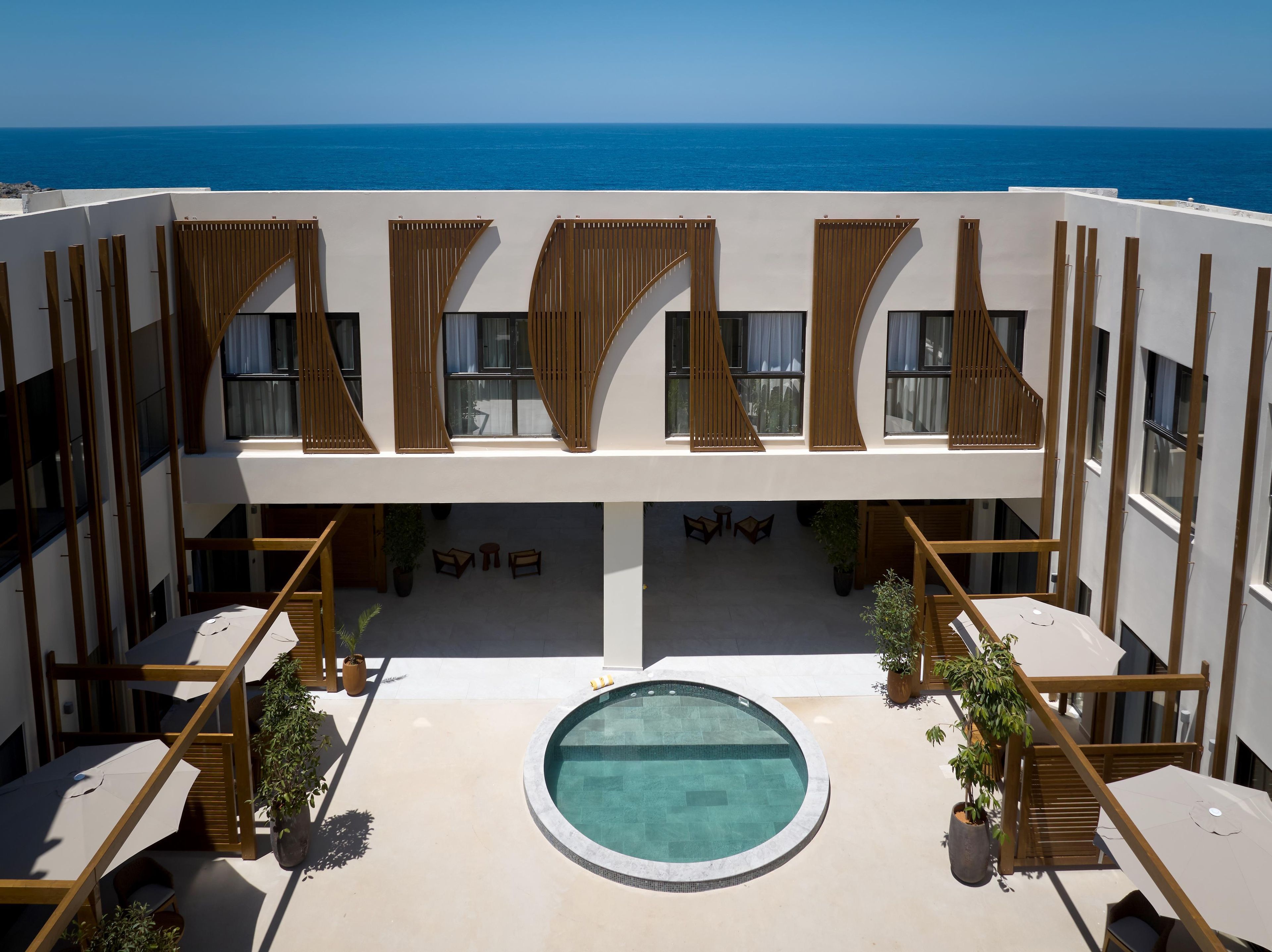 Zona de piscina en la azotea con vistas al mar, ventanas de listones de madera y mobiliario exterior.