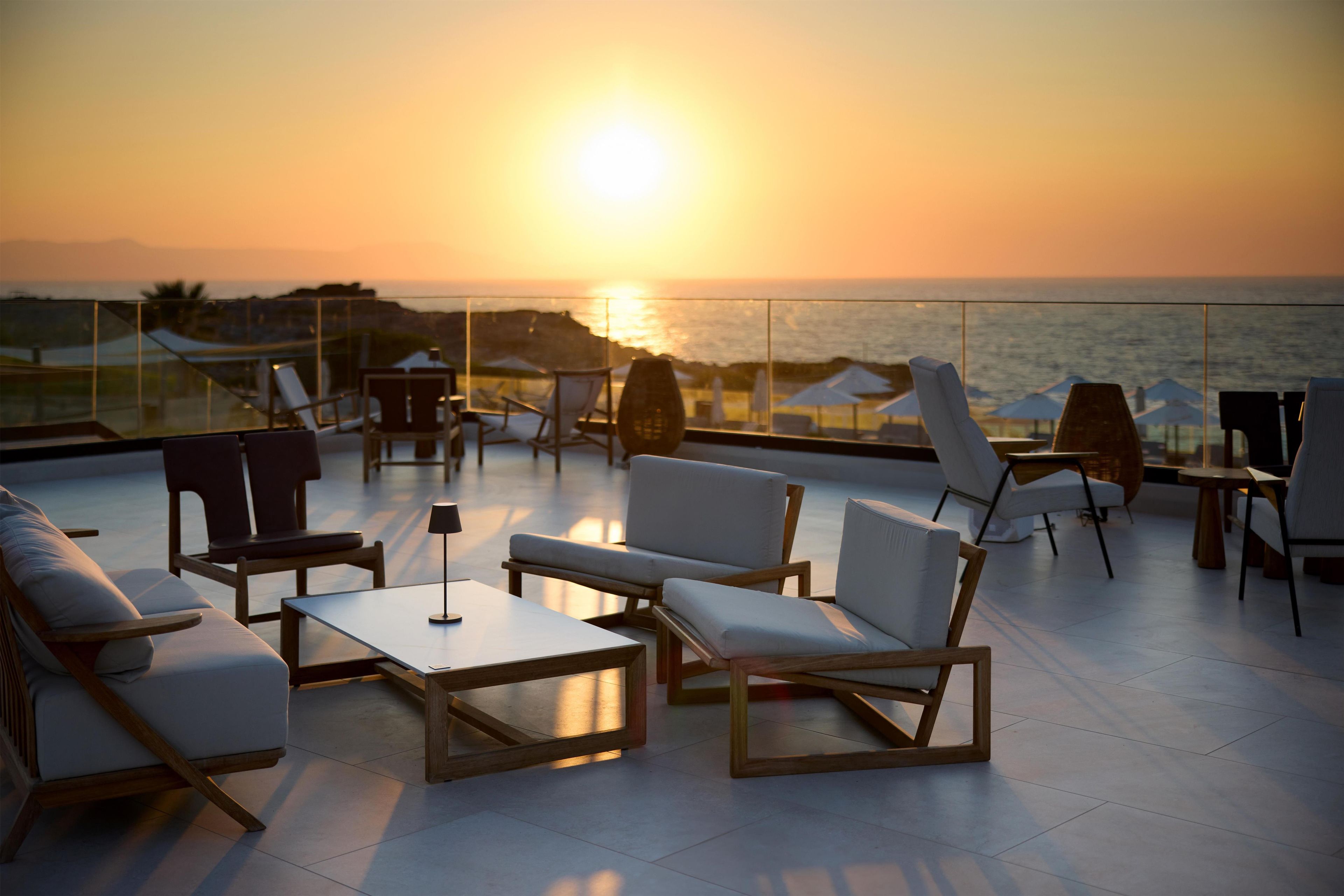 A terrace with seating and tables, overlooking a sunset over the sea.