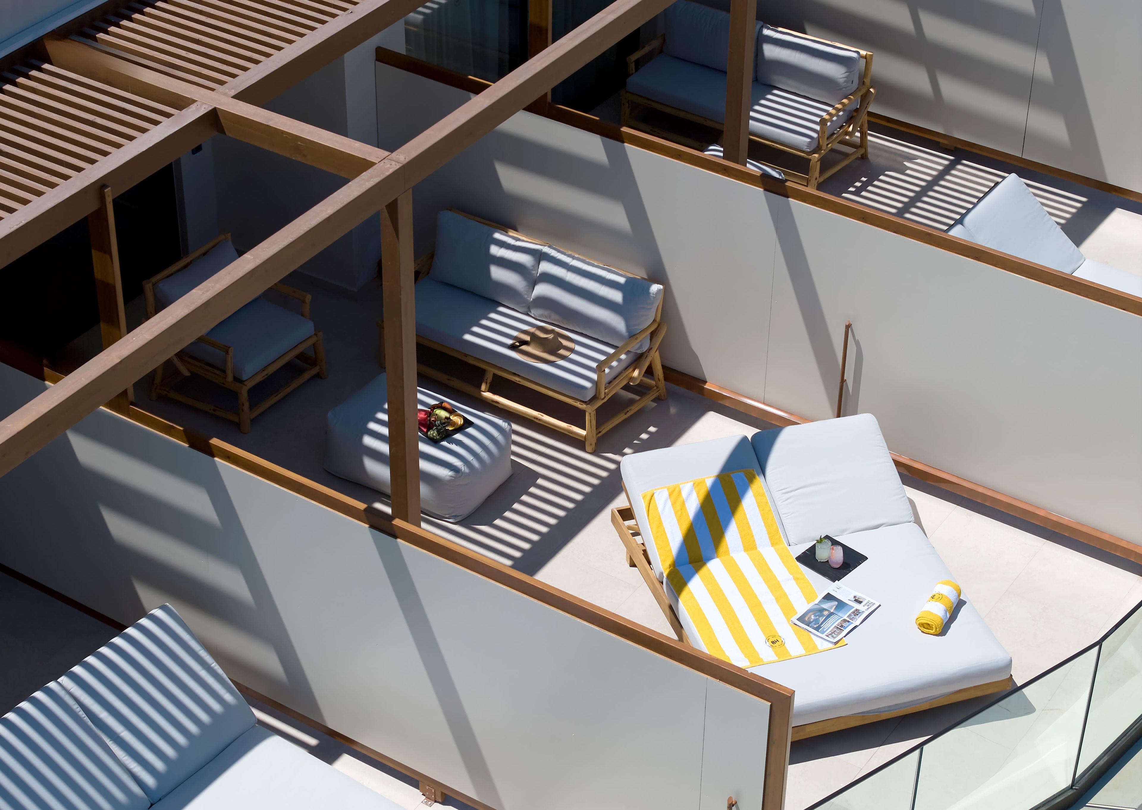 A sunlit outdoor seating area with multiple lounge chairs and a sofa, arranged on a terrace with a view of the surrounding area.
