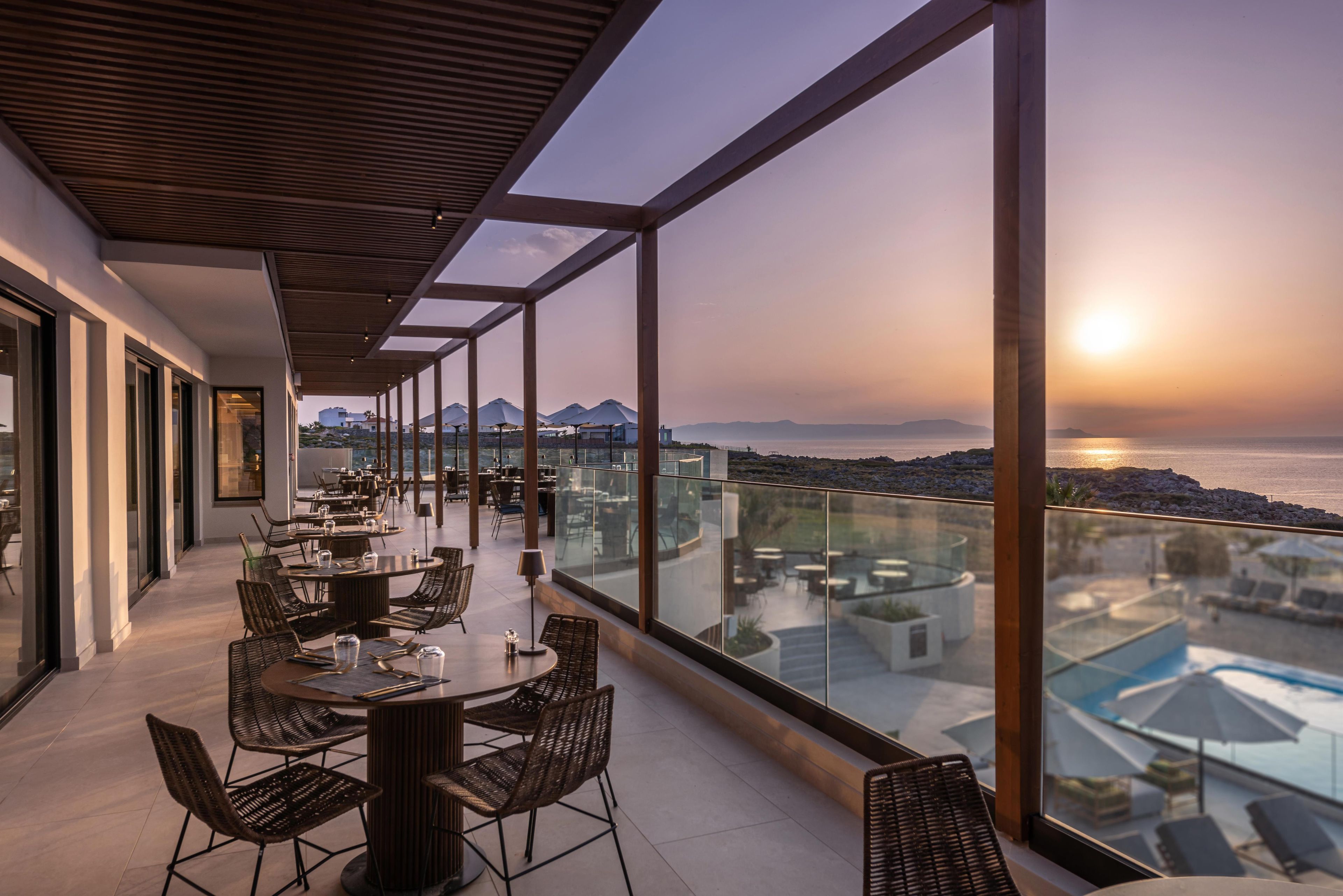 A modern outdoor dining area with large windows overlooking a pool and mountains.