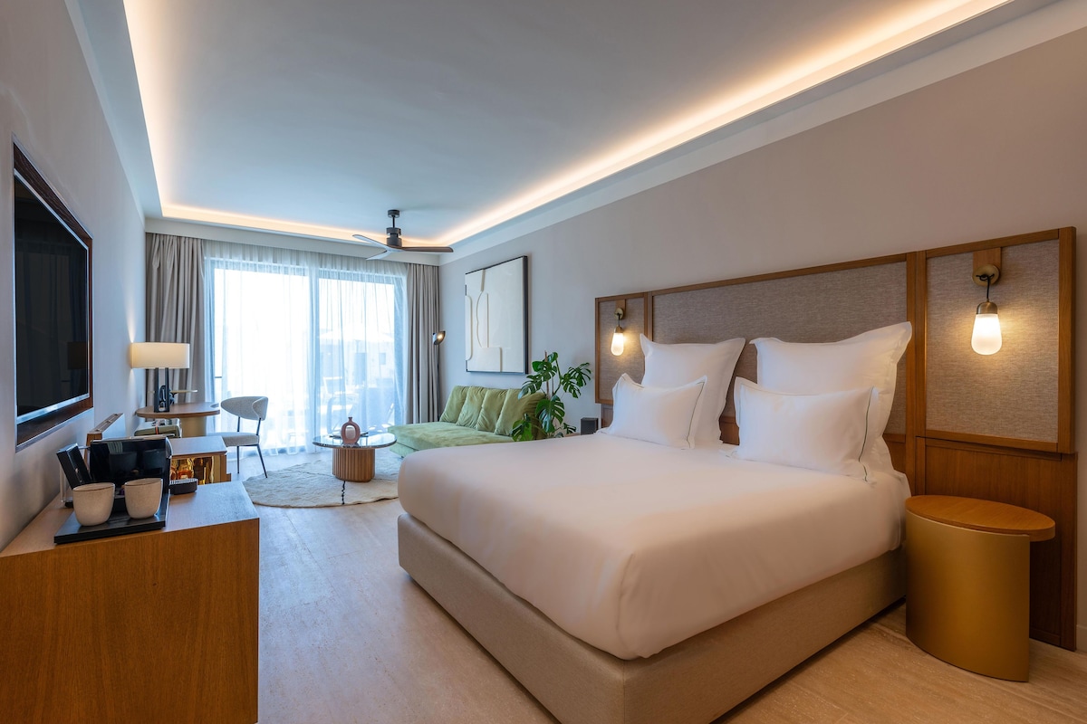 A modern hotel room with a large bed, a desk, a chair, and a TV.