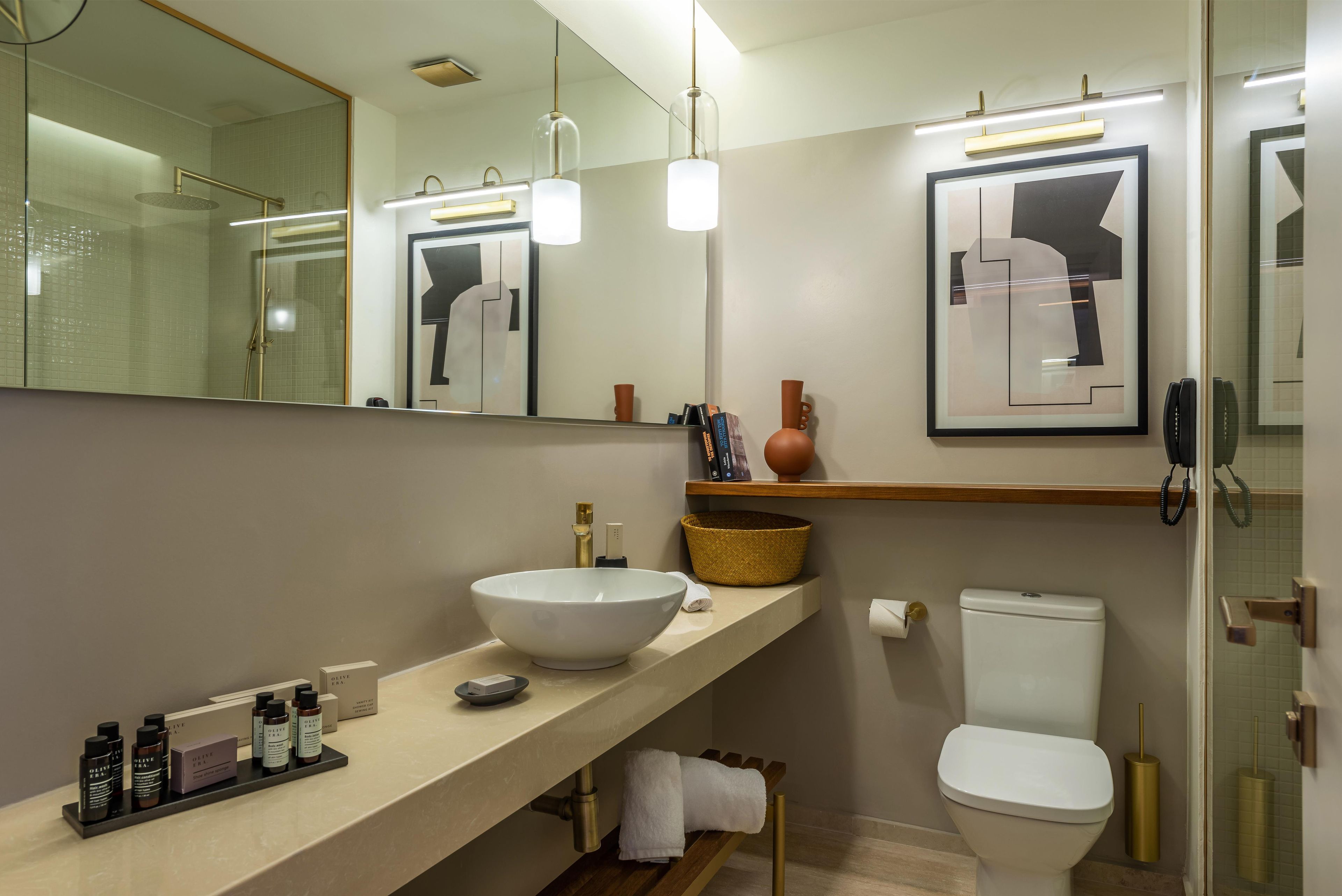 A modern bathroom with a large mirror, a white sink, a toilet, and a shower area.