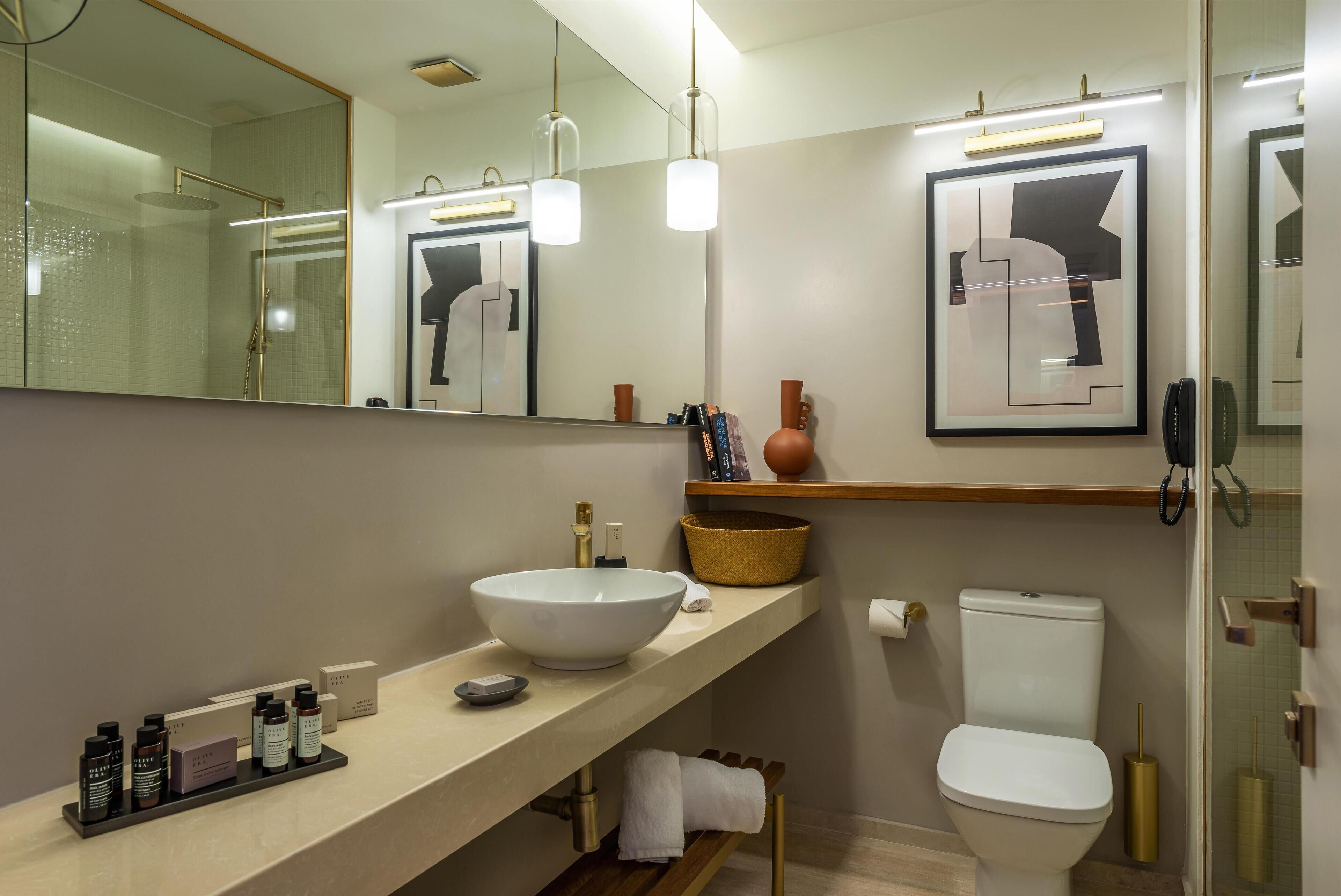 A modern bathroom with a large mirror, a white sink, a toilet, and a shower area.
