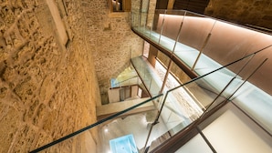 Un interior de varios niveles con paredes de piedra, barandas de cristal y una escalera moderna.